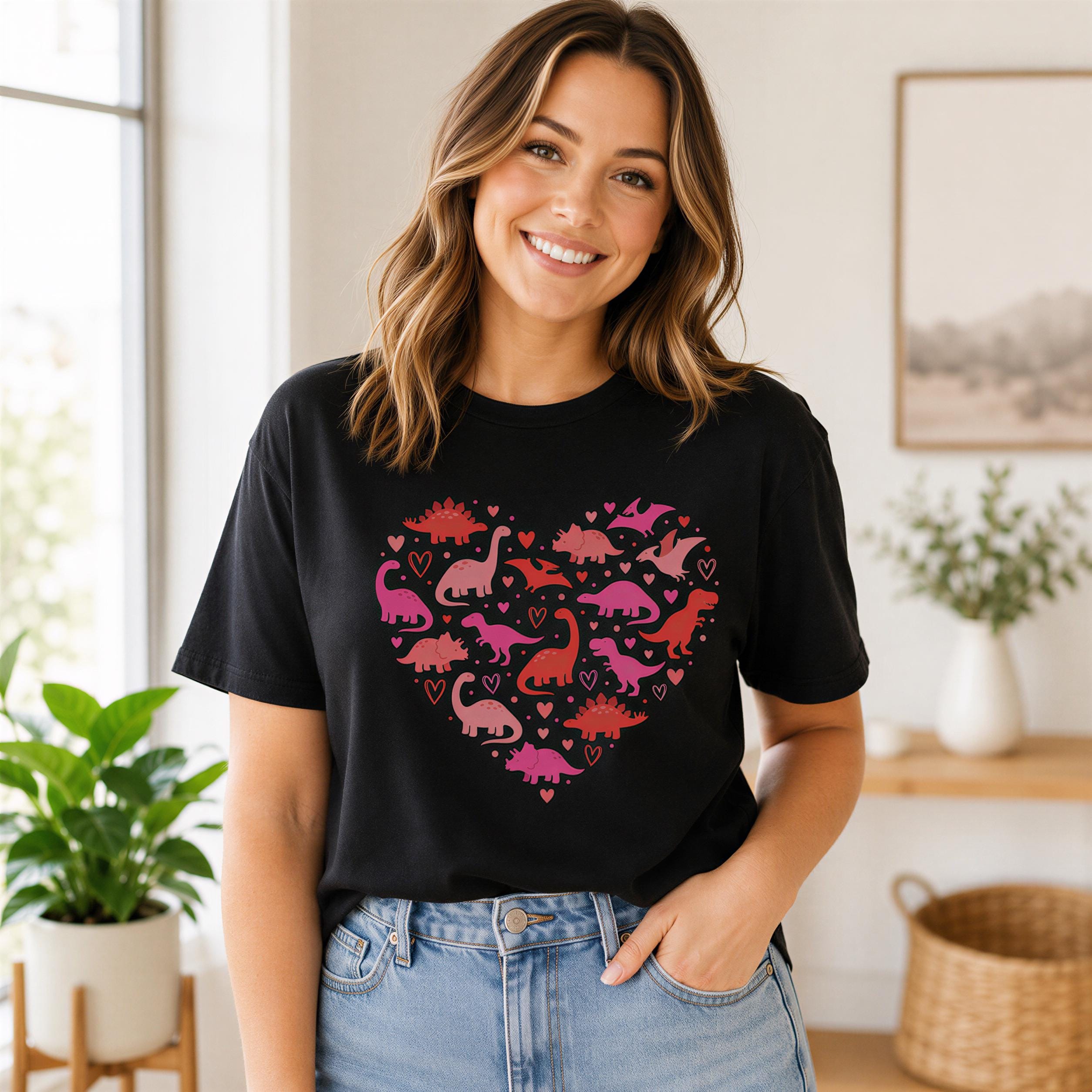 A woman wearing a black t-shirt with a heart-shaped design featuring pink and red dinosaurs and hearts, smiling at the camera.