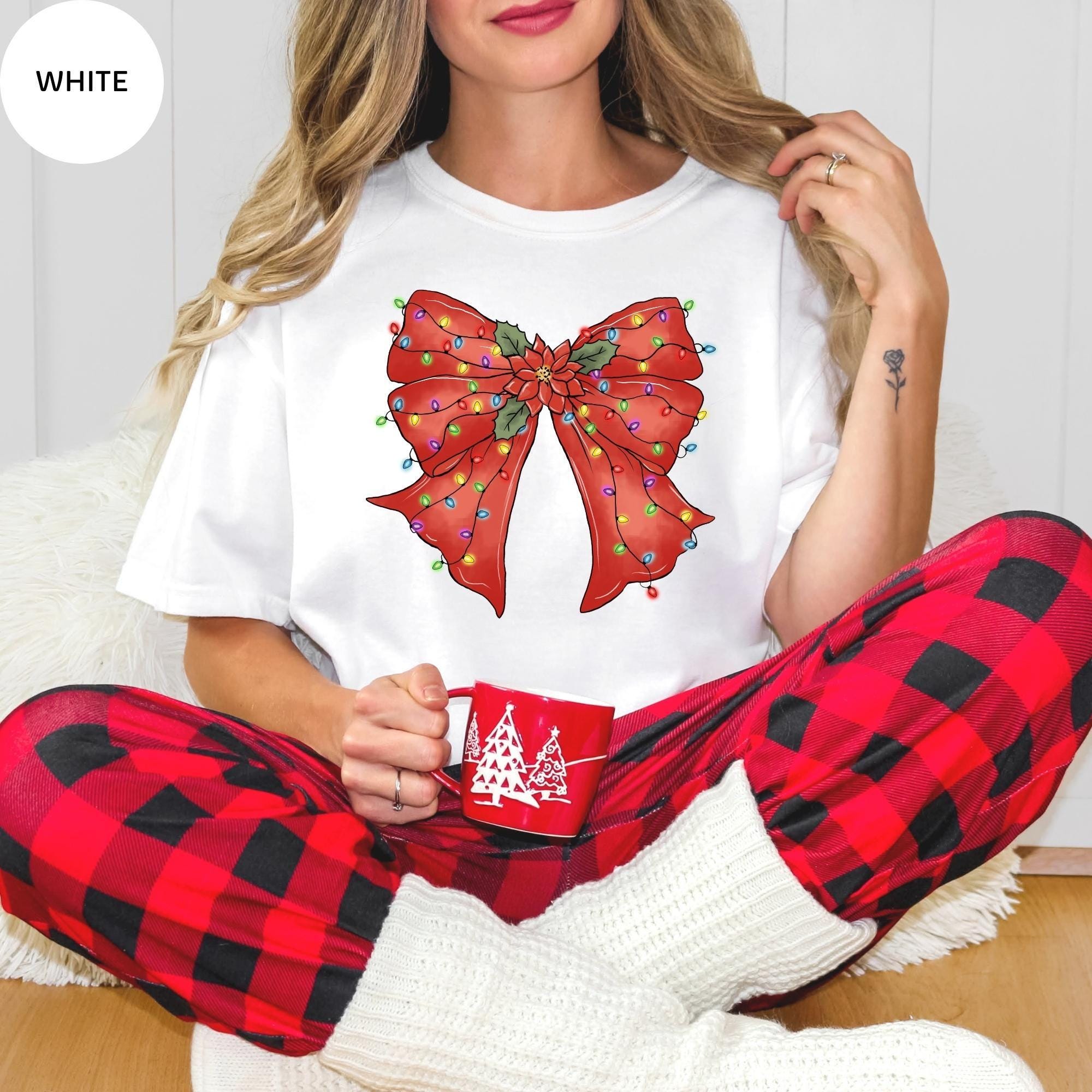 A woman wearing a white t-shirt with a red bow and red and white plaid pants, holding a red mug with a Christmas tree design.