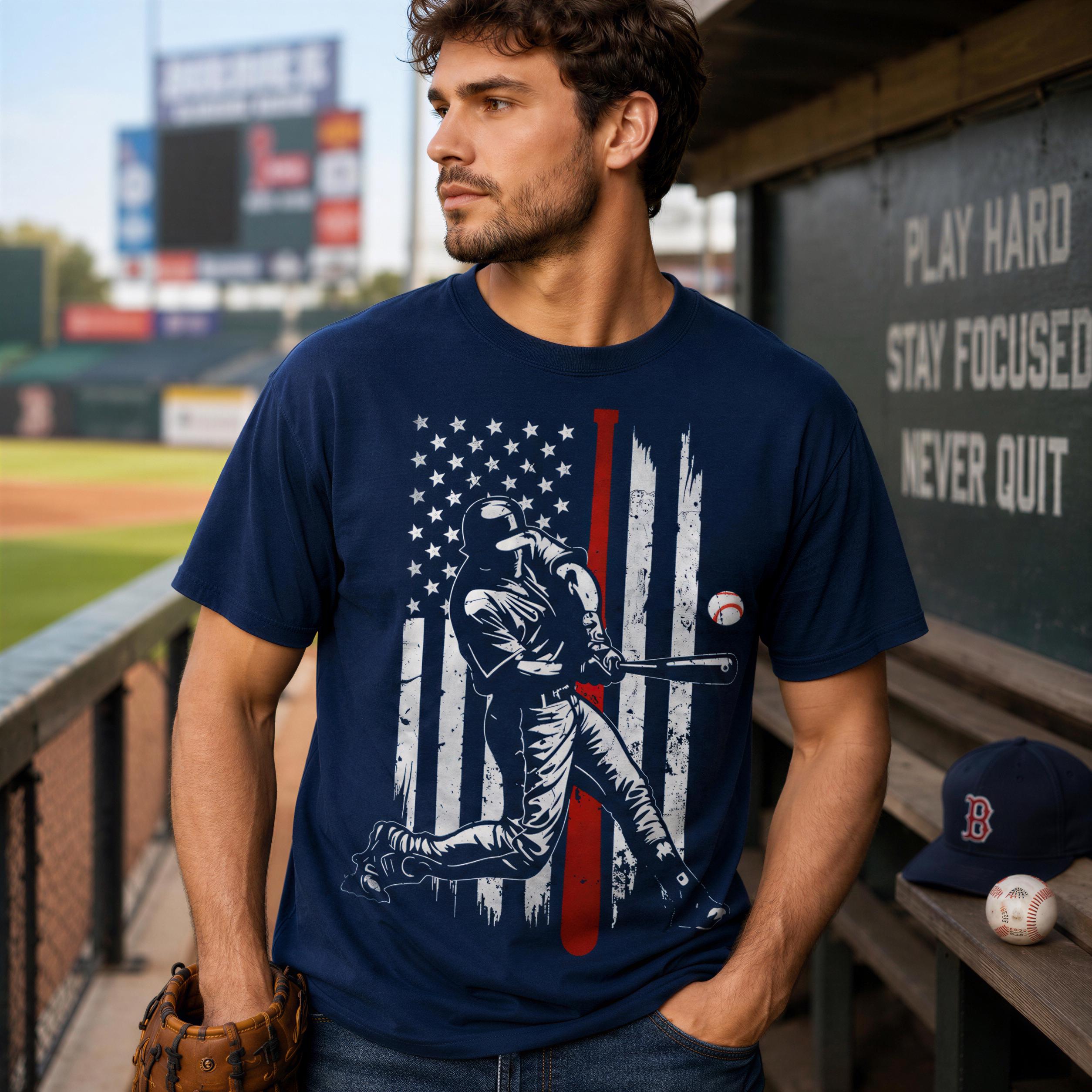 A man wearing a navy blue t-shirt with an American flag design and a baseball graphic stands in a baseball field.