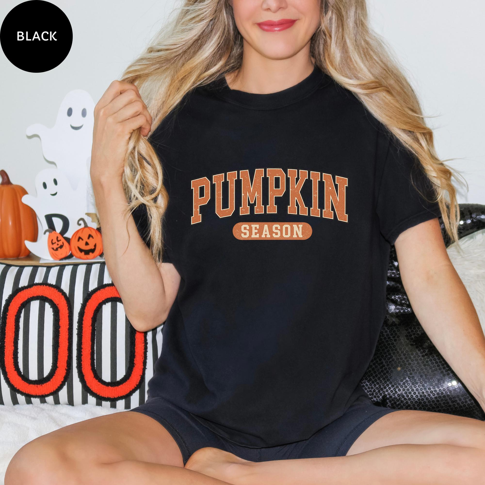 A woman wearing a black t-shirt with the text "PUMPKIN SEASON" is sitting on a couch, surrounded by Halloween decorations.