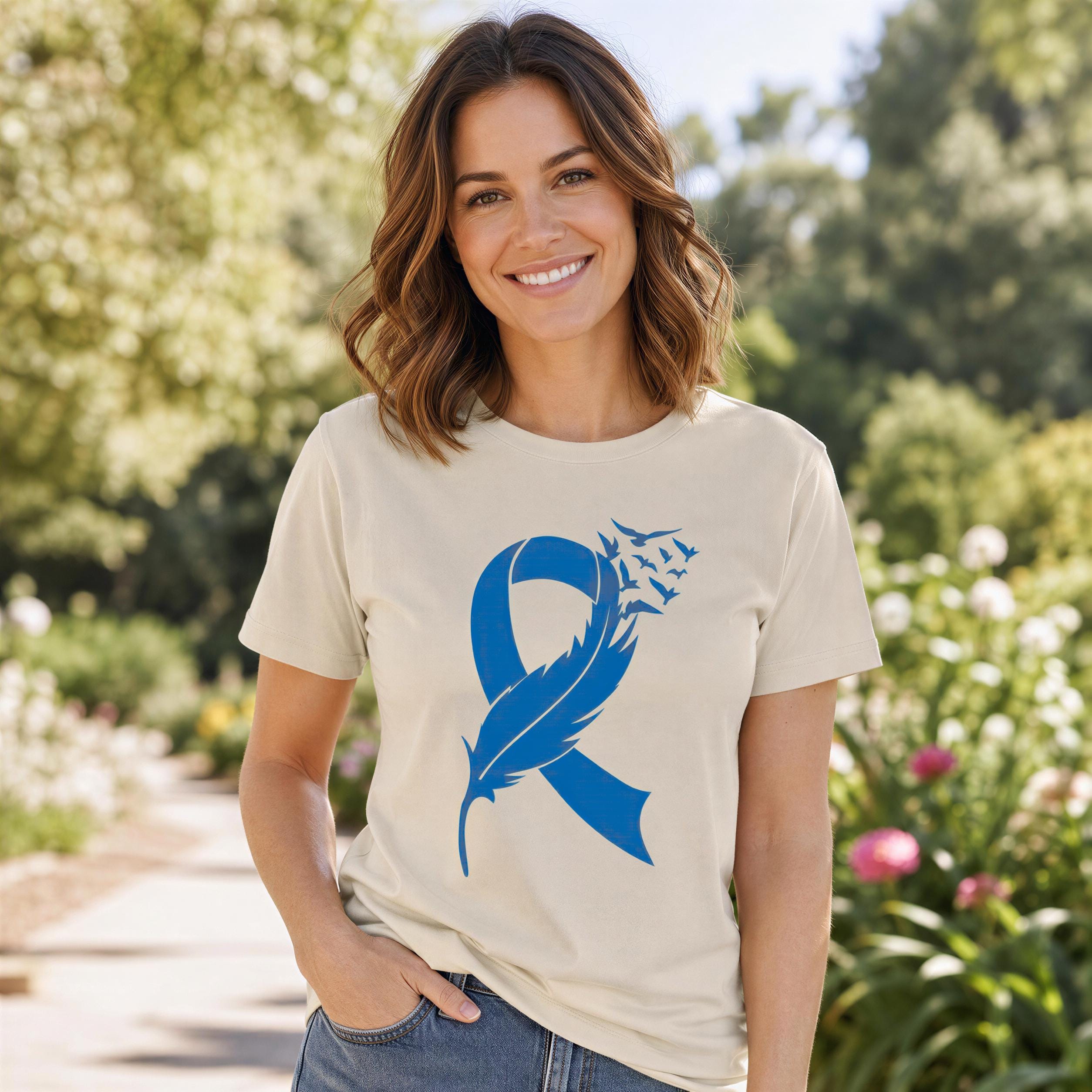 A woman wearing a white t-shirt with a blue feather design stands in a garden surrounded by flowers.