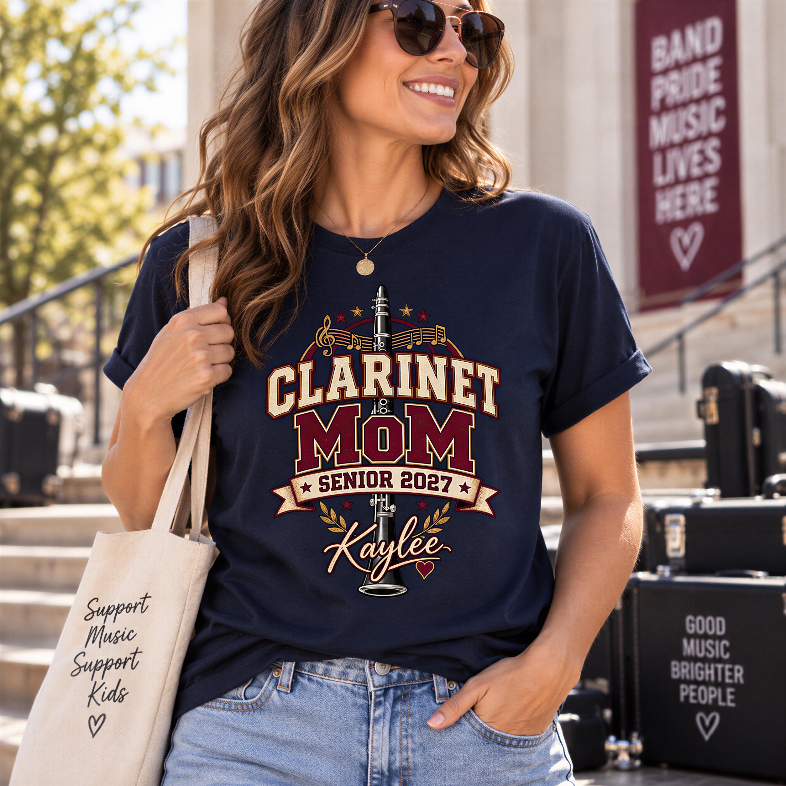 A woman wearing a navy blue t-shirt with a graphic design, smiling and holding a beige tote bag.