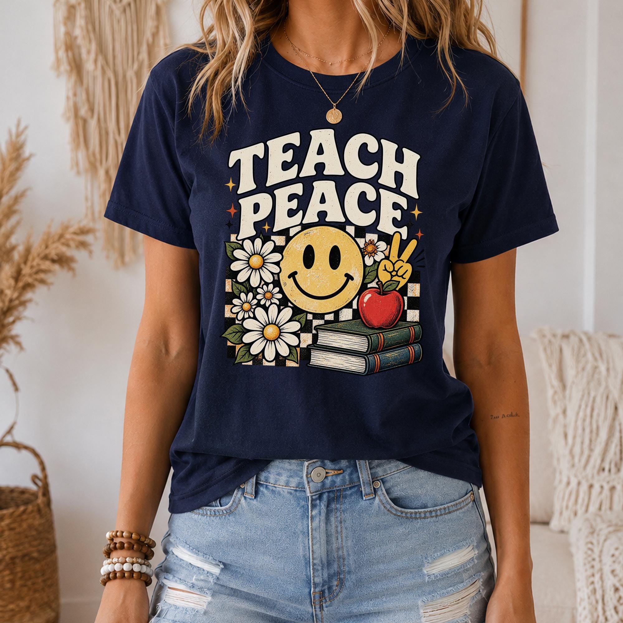 A woman wearing a navy blue t-shirt with a graphic design that says "Teach Peace" and features a smiling face, flowers, books, and a peace sign.
