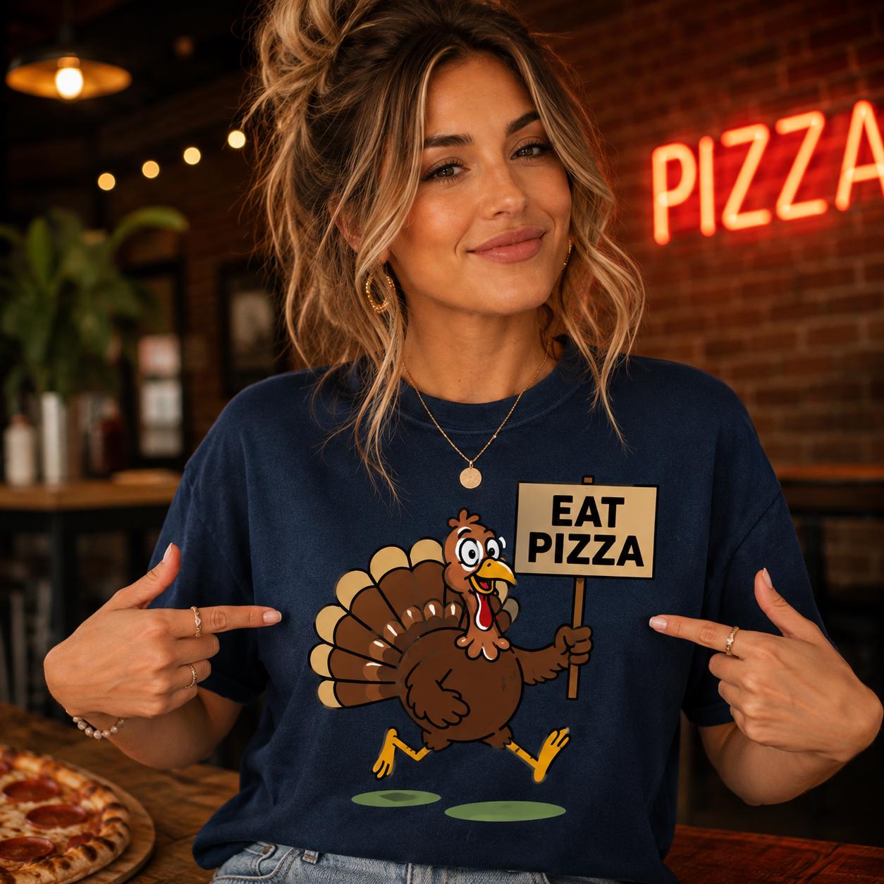 A woman wearing a blue t-shirt with a cartoon turkey holding a sign that says "EAT PIZZA" is smiling and pointing at the sign.