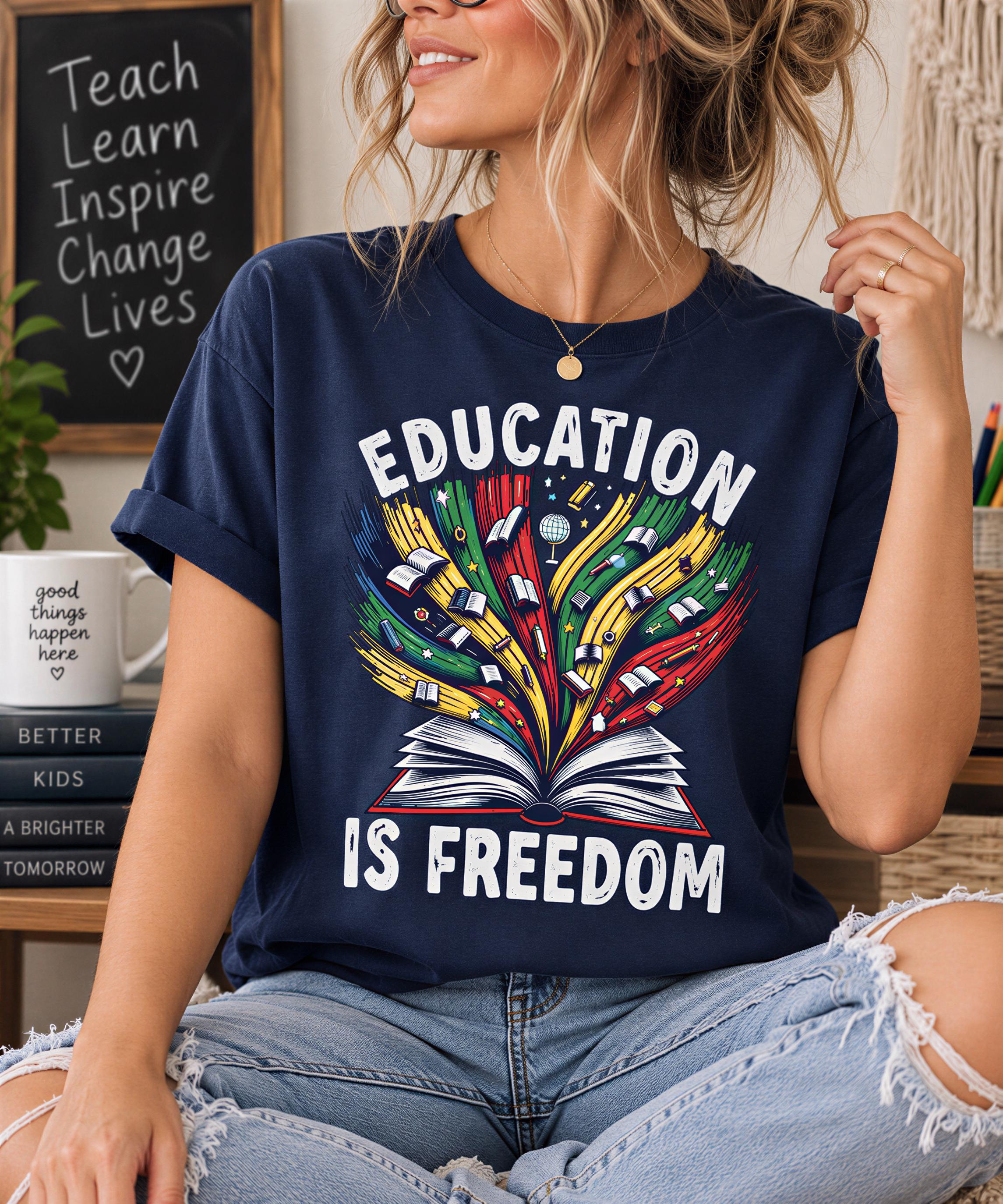 A woman wearing a blue t-shirt with a graphic design of an open book and colorful illustrations, sitting in a casual setting with a chalkboard sign in the background.