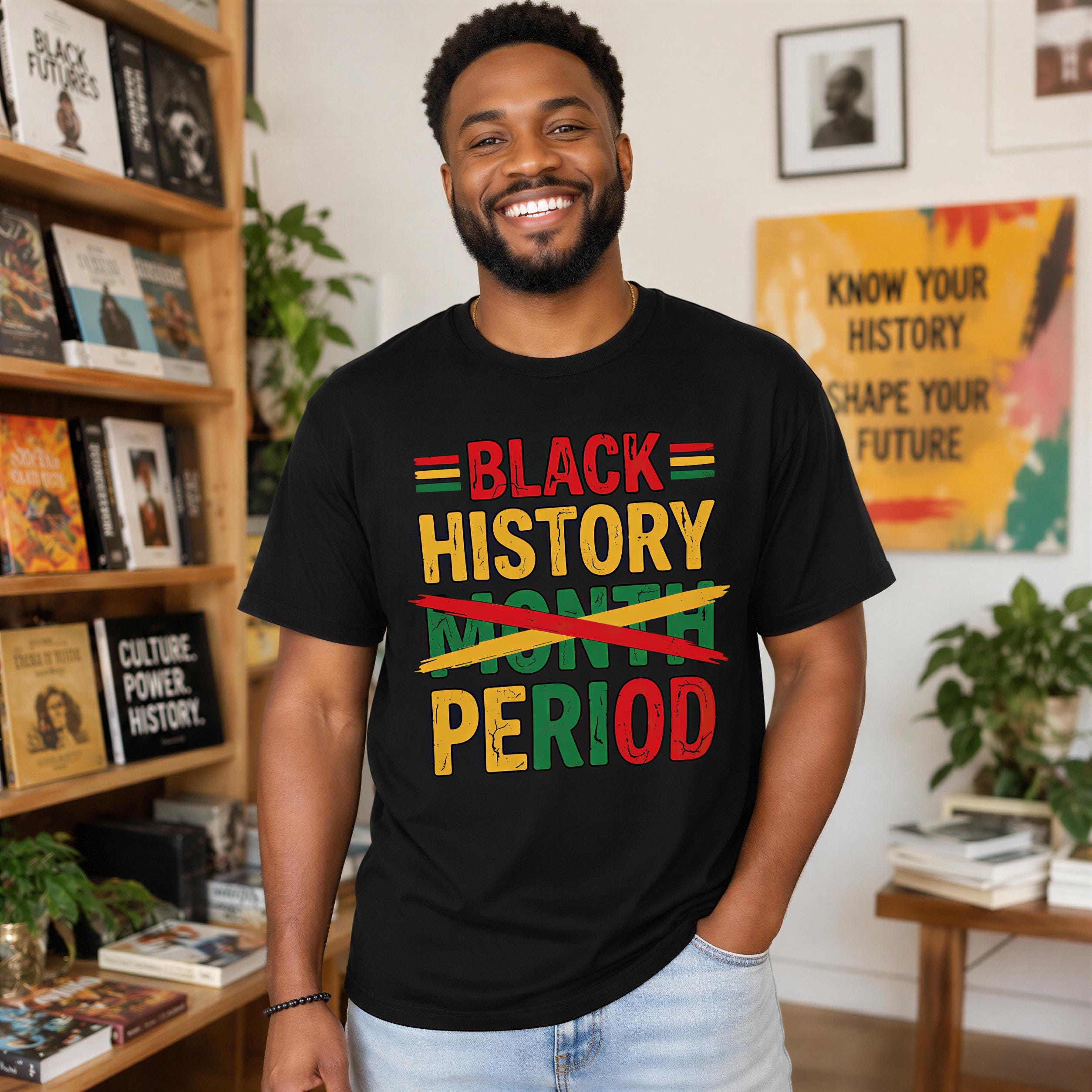 A smiling man wearing a black t-shirt with text printed on it stands in a room with bookshelves and plants in the background.