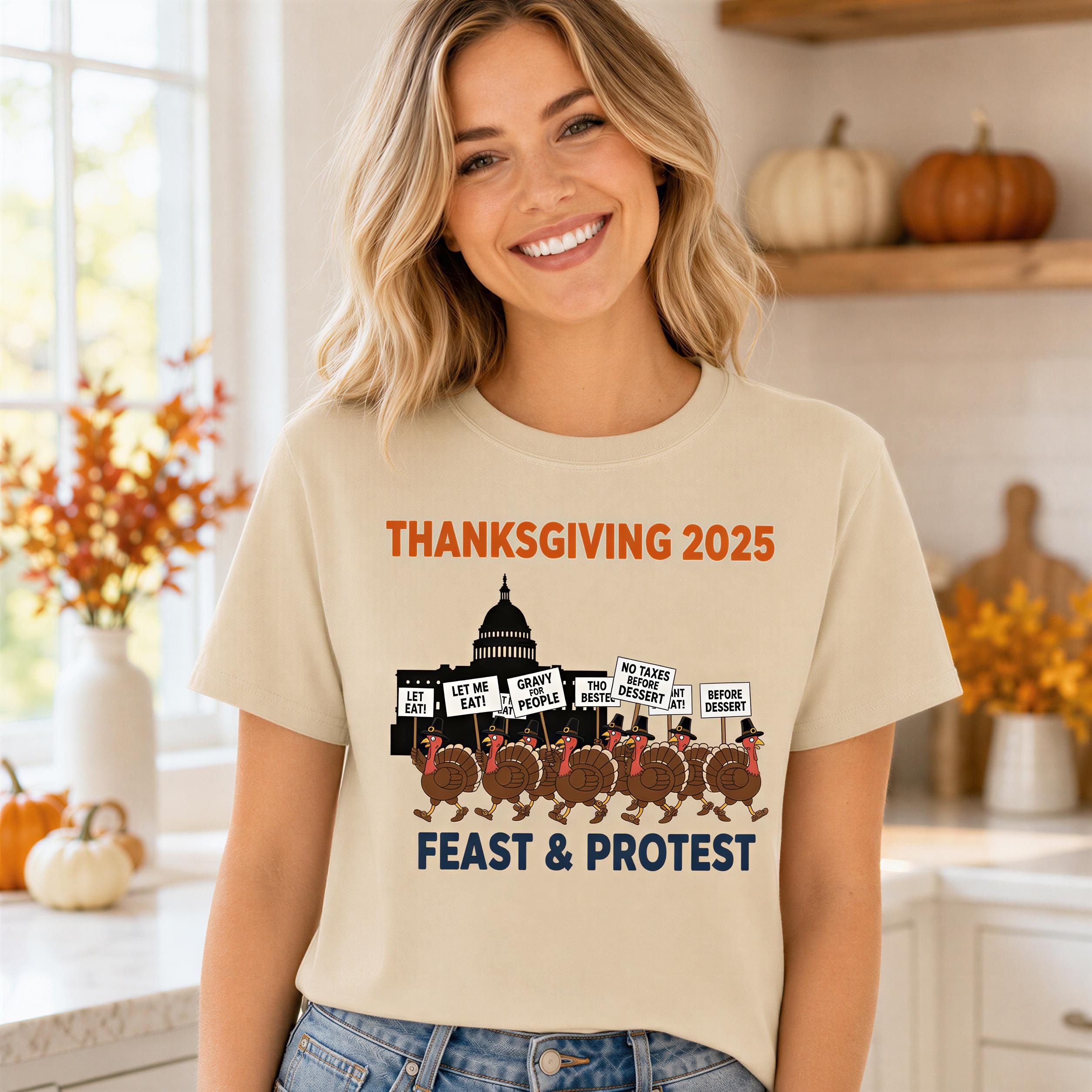 A woman wearing a t-shirt with a graphic design depicting a protest with a group of people holding signs, including one that says "No Taxes. Let me eat. Let me protest."