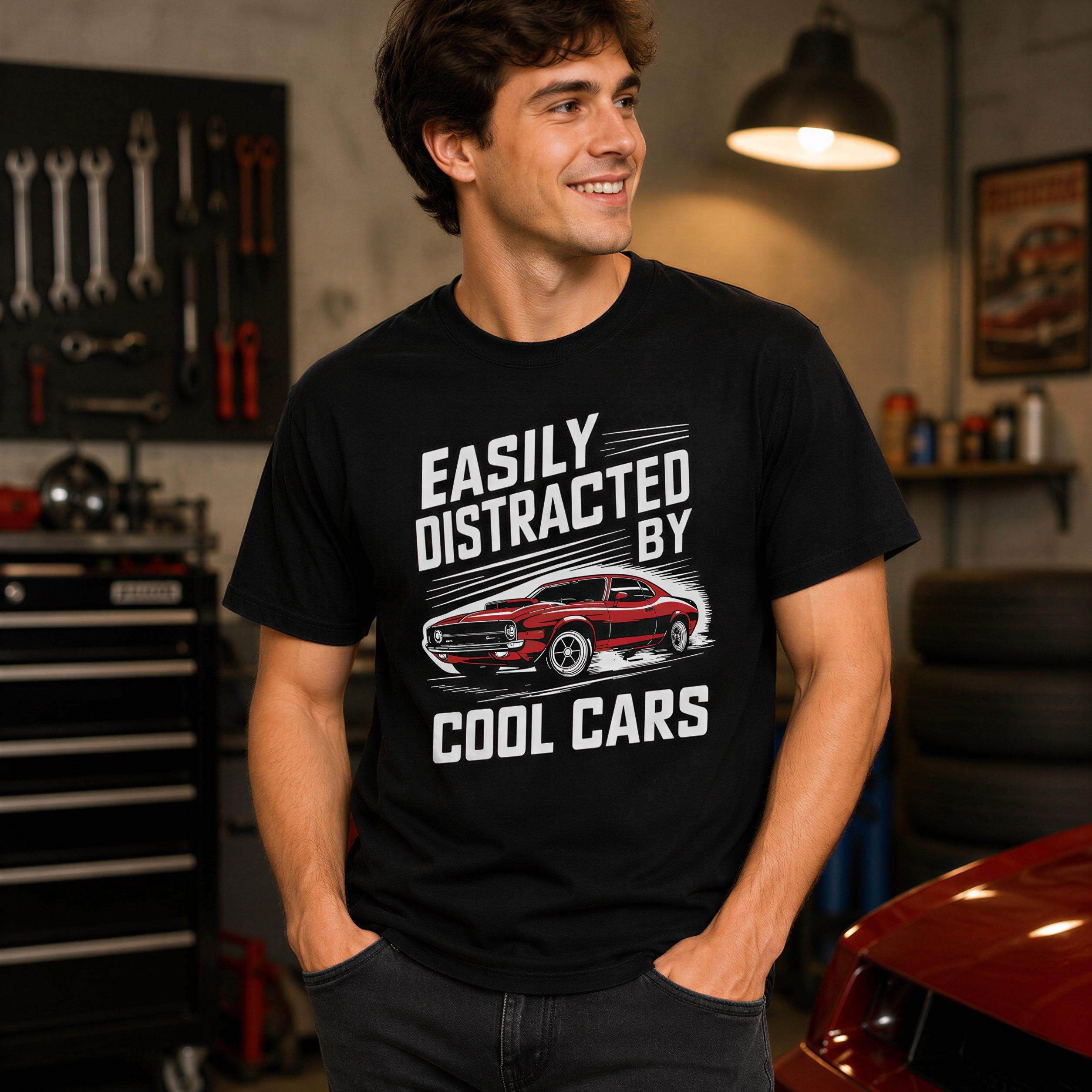 A man wearing a black t-shirt with a graphic of a red car and the text "EASILY DISTracted BY COOL CARS" is standing in a garage with various tools and equipment visible in the background.