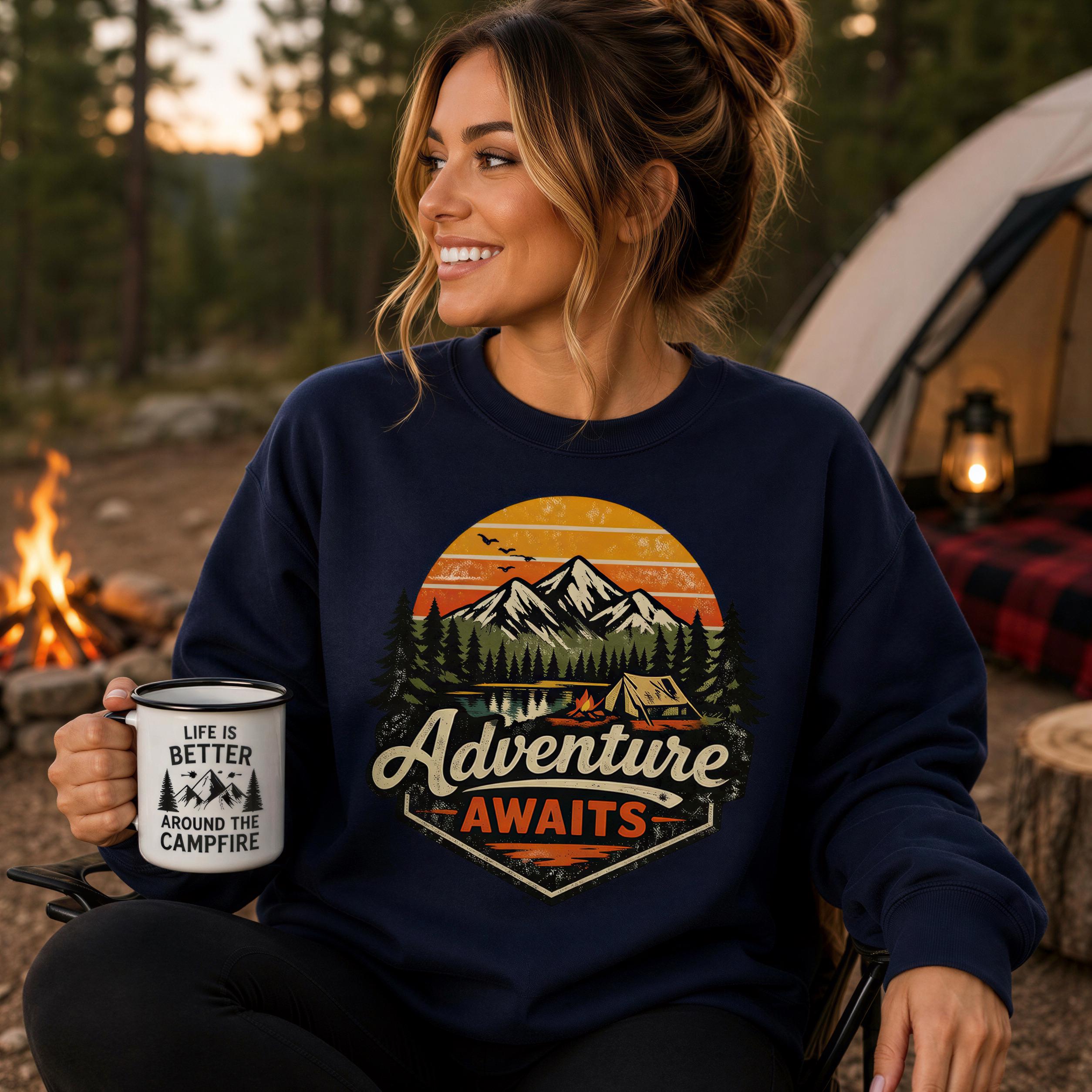 A woman wearing a blue sweatshirt with a graphic design of a mountain landscape and camping tents, holding a mug with the text "Life is better around the campfire".