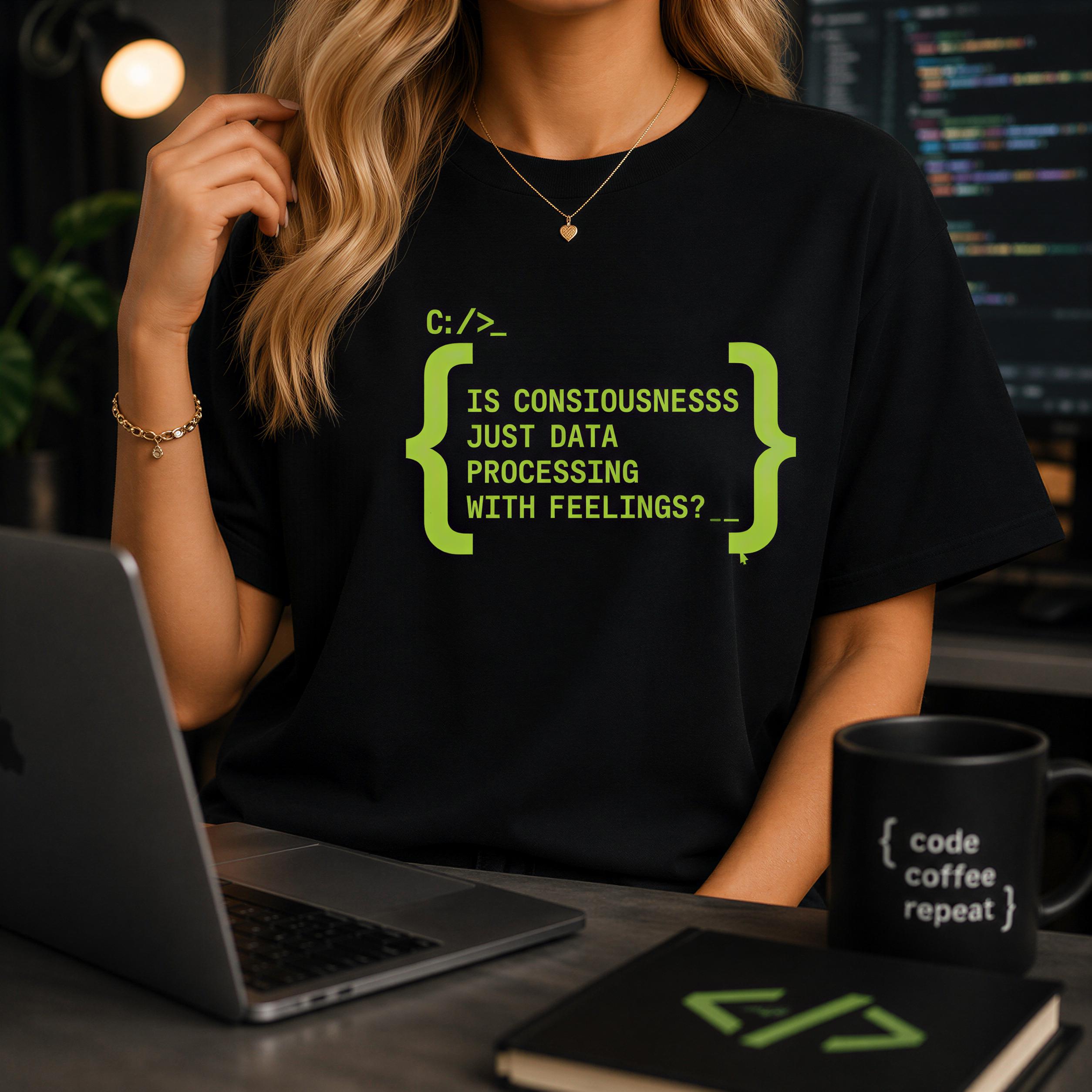 A person wearing a black t-shirt with a humorous programming-themed graphic is sitting at a desk with a laptop, a coffee mug, and a notebook.