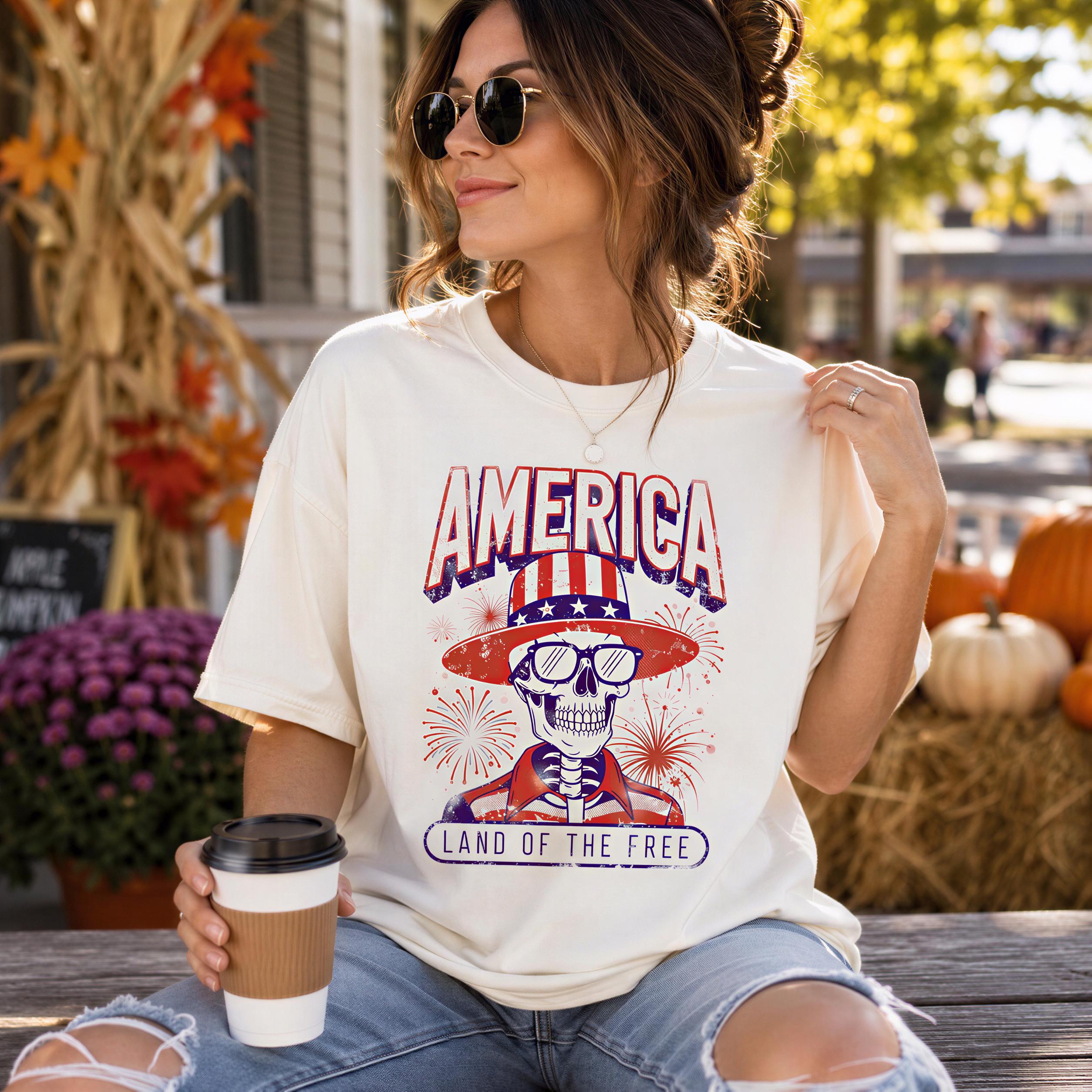 A woman wearing a white t-shirt with a graphic design of a skeleton wearing a hat and sunglasses, holding a coffee cup and sitting on a bench.