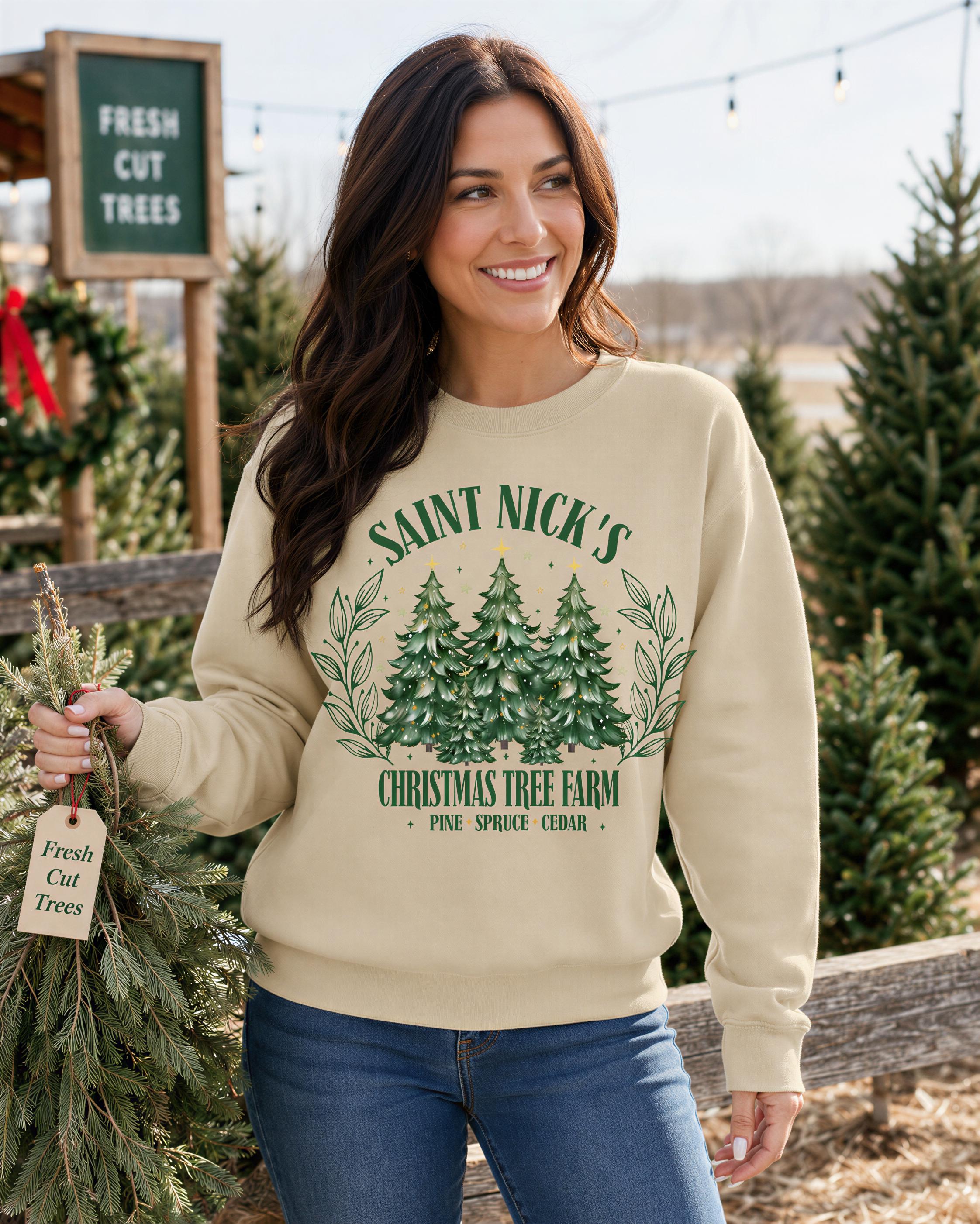 A woman wearing a beige sweater with a Christmas tree design stands in front of a Christmas tree farm, holding a small evergreen tree.