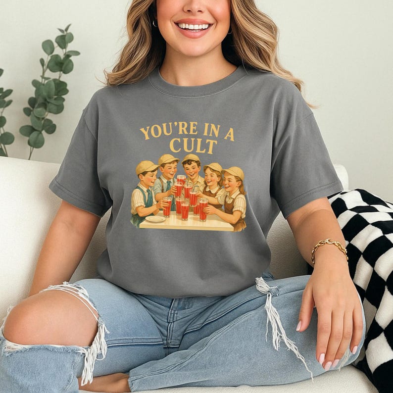 A woman wearing a gray t-shirt with a graphic design of a group of people enjoying drinks at a table.