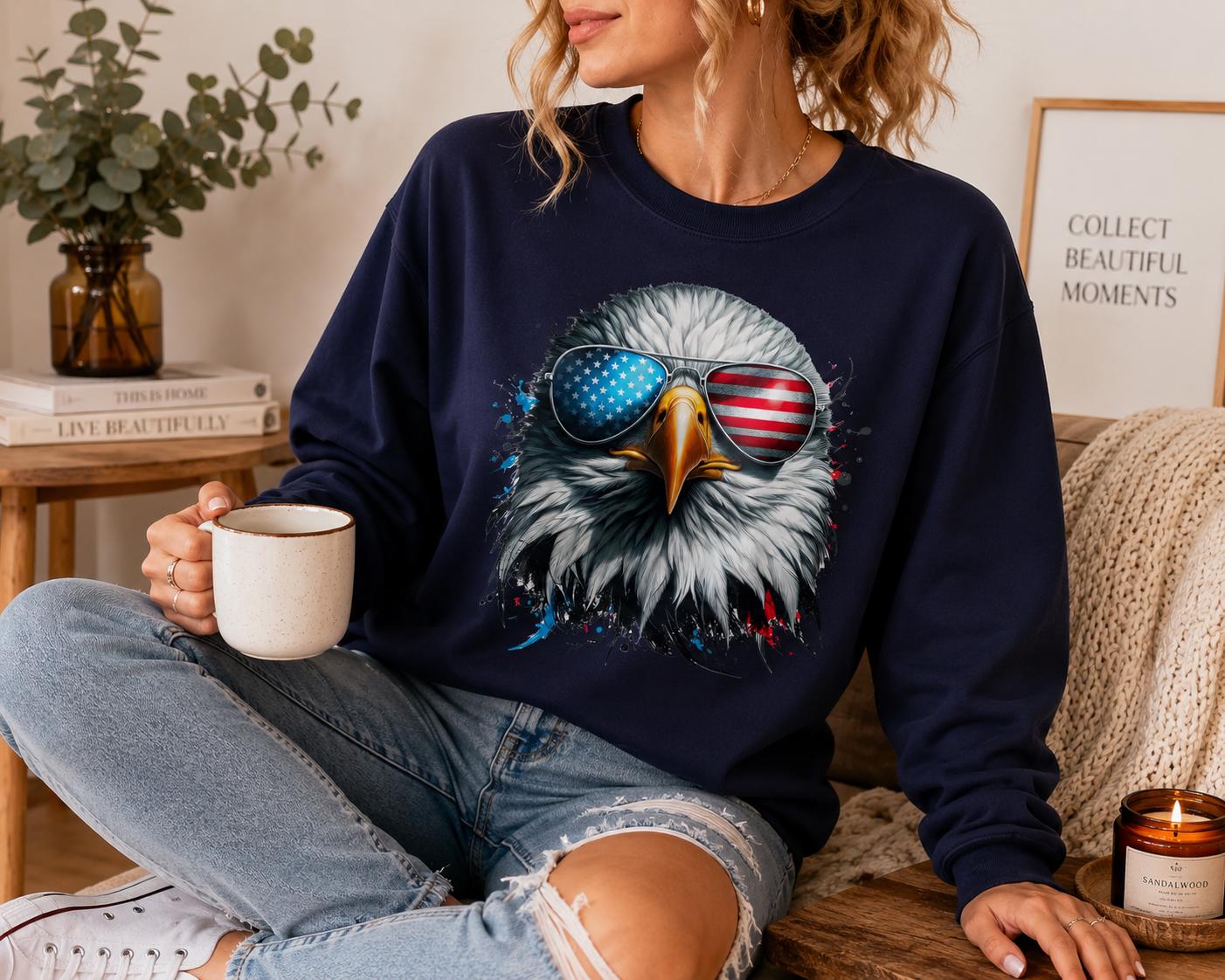 A woman wearing a navy blue sweatshirt with an eagle design and sunglasses is sitting on a couch, holding a coffee mug and a candle.
