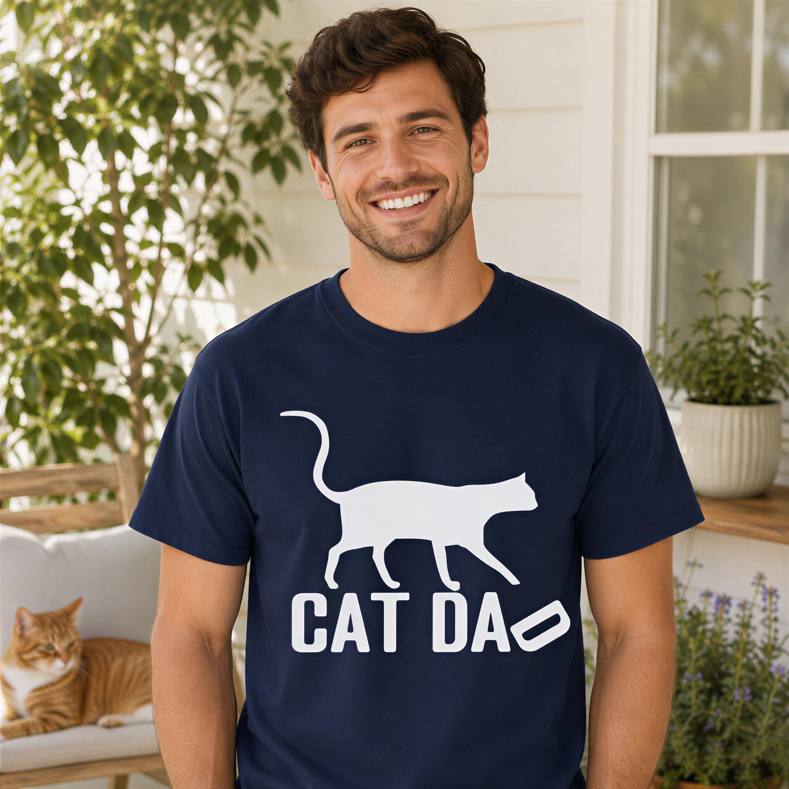 A man wearing a navy blue t-shirt with a white cat graphic and the text "CAT DA" is smiling and posing for the camera.