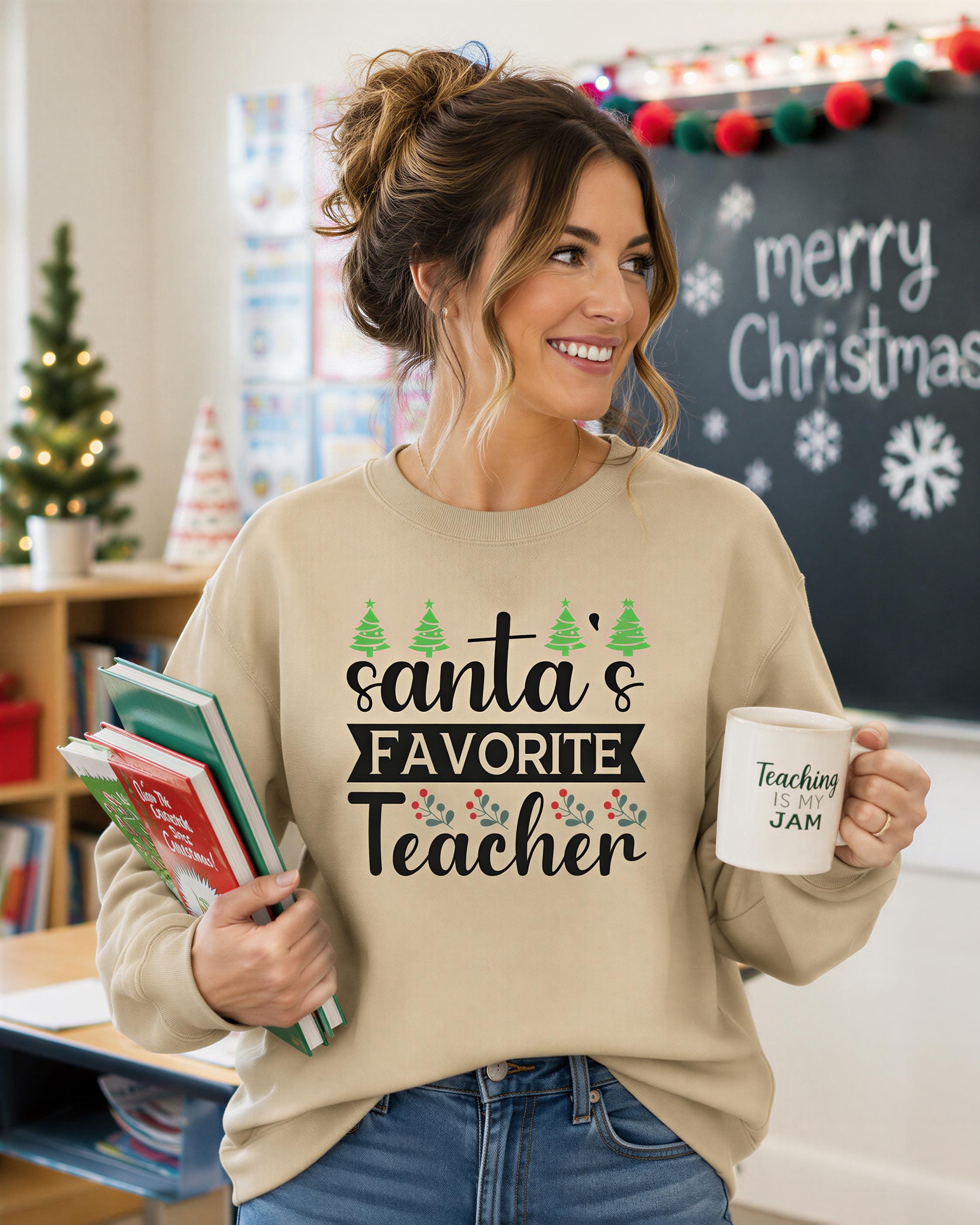 A woman wearing a beige sweater with the text "Santa's Favorite Teacher" is holding a stack of books and a mug with the text "Teaching is my jam" in front of a Christmas tree and a chalkboard with the text "Merry Christmas".