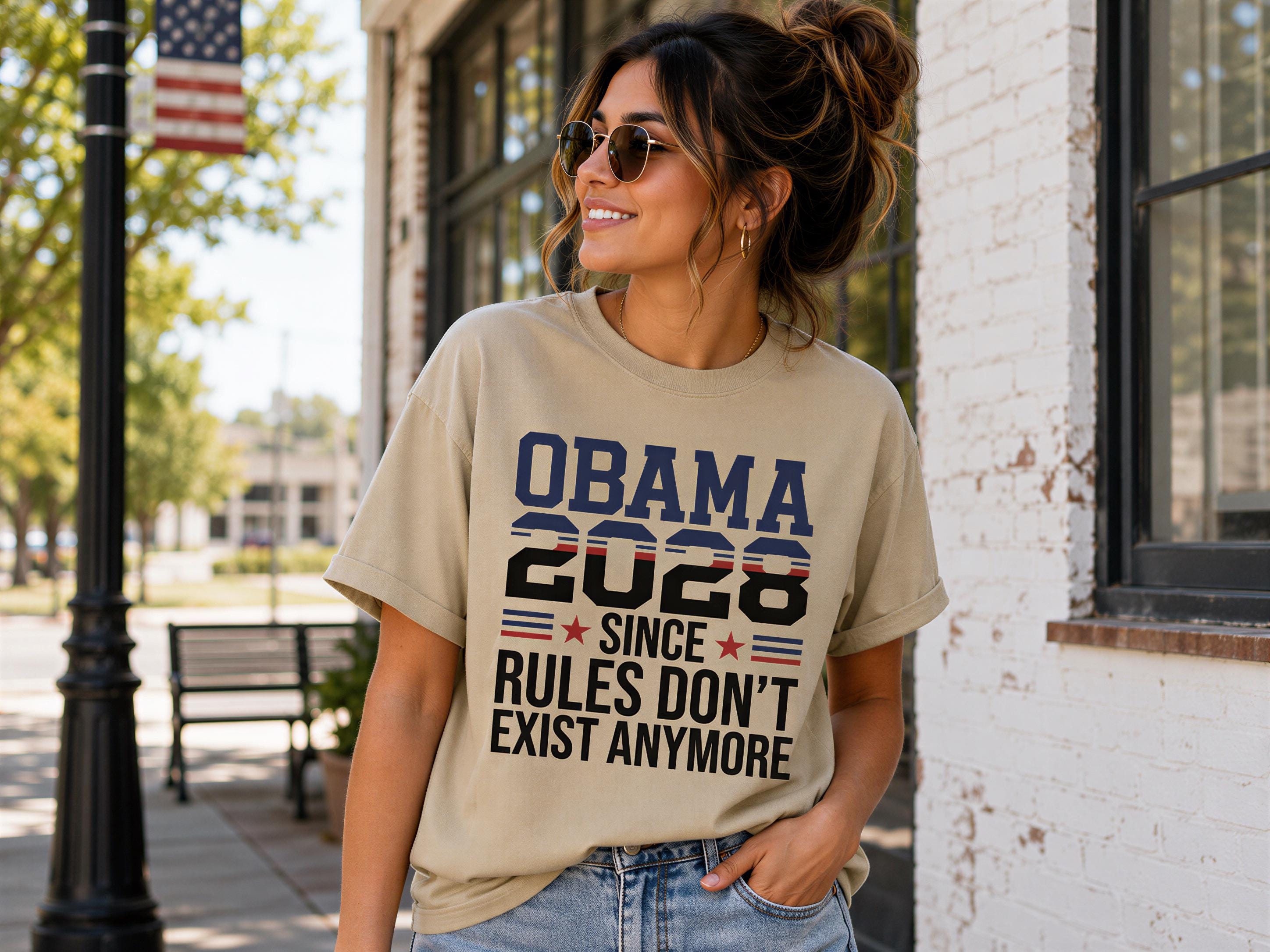 A woman wearing a t-shirt with the text "OBAMA 2020 SINCE RULES DON'T EXIST ANYMORE" is standing on a sidewalk.