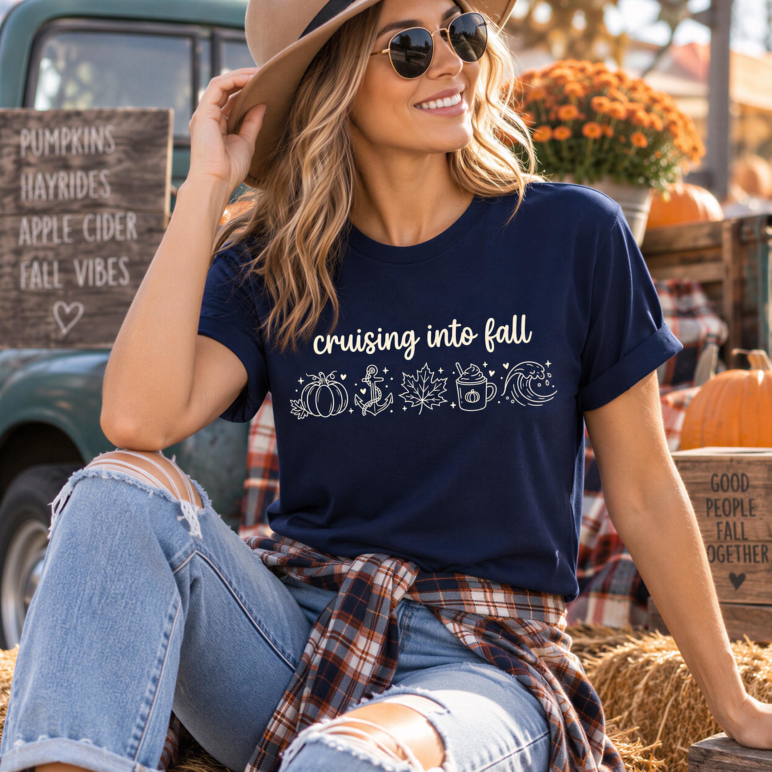 A woman wearing a blue t-shirt with the text "Cruising into fall" and sunglasses is sitting on a hay bale, smiling and looking at the camera.