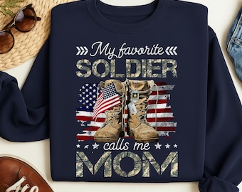 Può includere: Felpa blu navy con la scritta "My favorite SOLDIER calls me MOM". Il design include una bandiera americana e stivali militari. Il testo e gli stivali hanno un motivo mimetico.