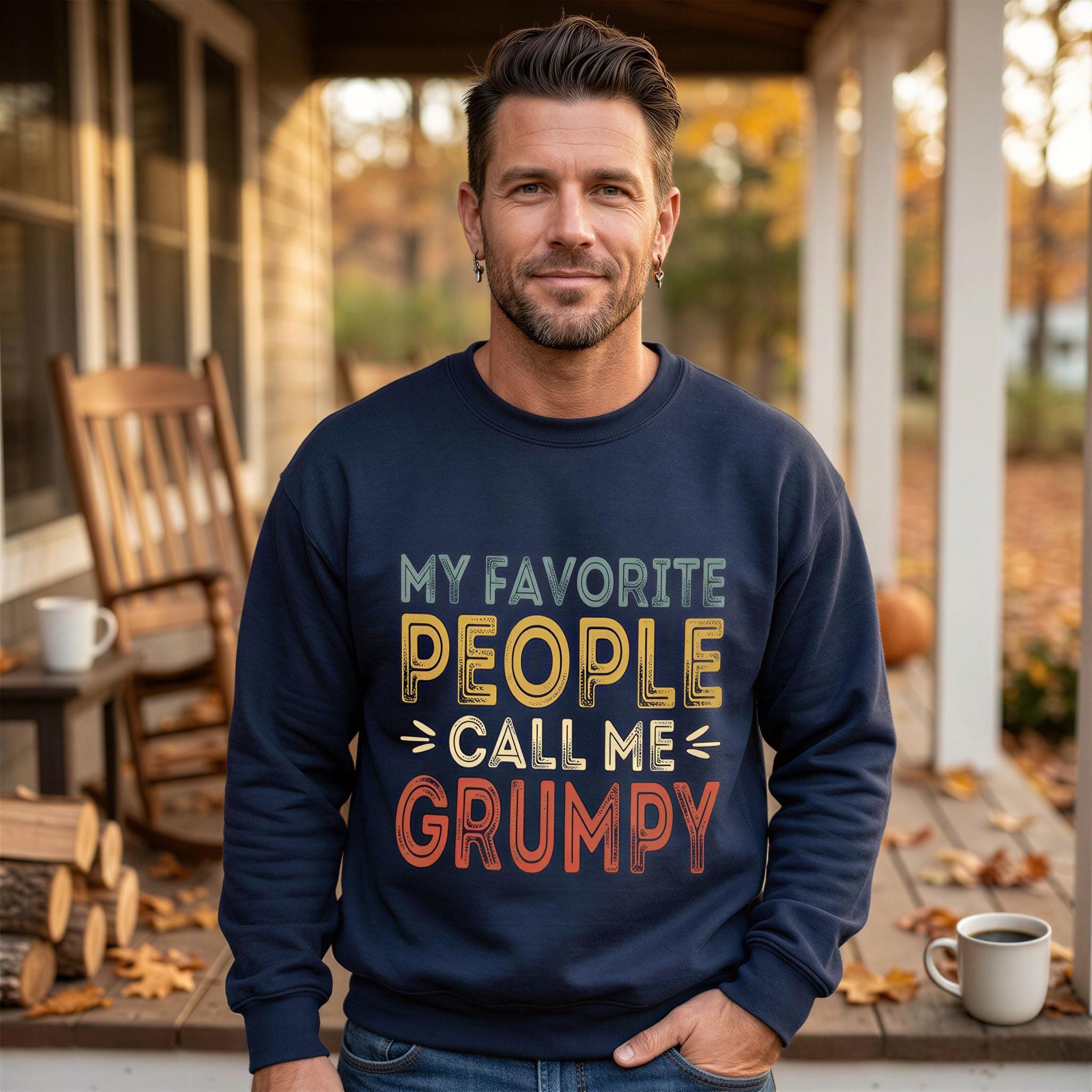 A man wearing a navy blue sweatshirt with the text "My favorite people call me grumpy" stands on a porch surrounded by autumn leaves.
