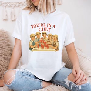 A woman wearing a white t-shirt with a graphic design of a group of people enjoying drinks together.