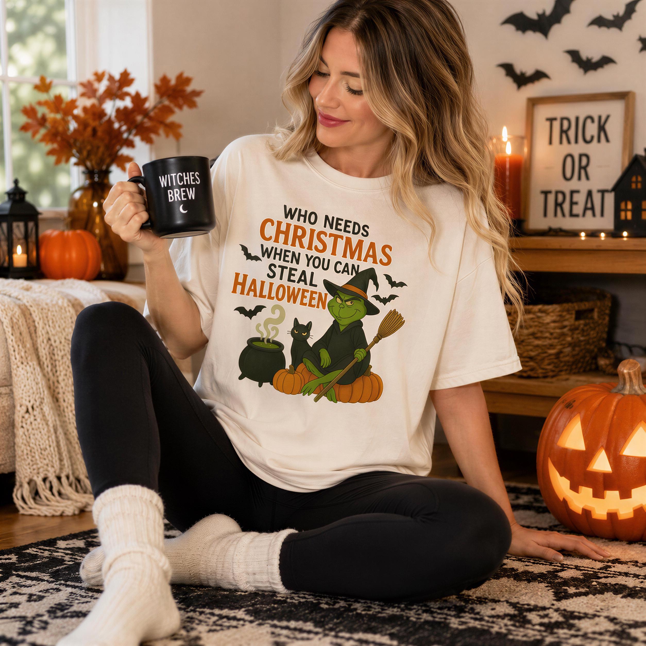 A woman sitting on the floor wearing a white t-shirt with a Halloween-themed graphic and holding a mug, surrounded by Halloween decorations and a carved jack-o-lantern.