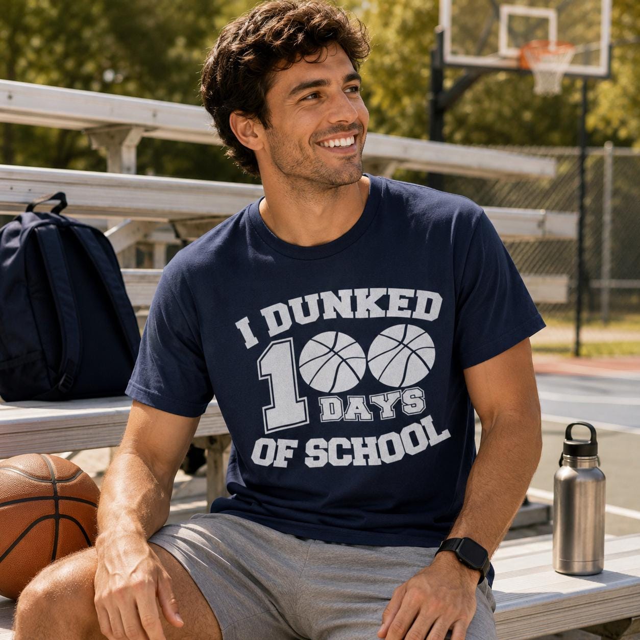 A man wearing a blue t-shirt with the text "I DUNKED 100 DAYS OF SCHOOL" is sitting on a bench with a basketball and a water bottle nearby.