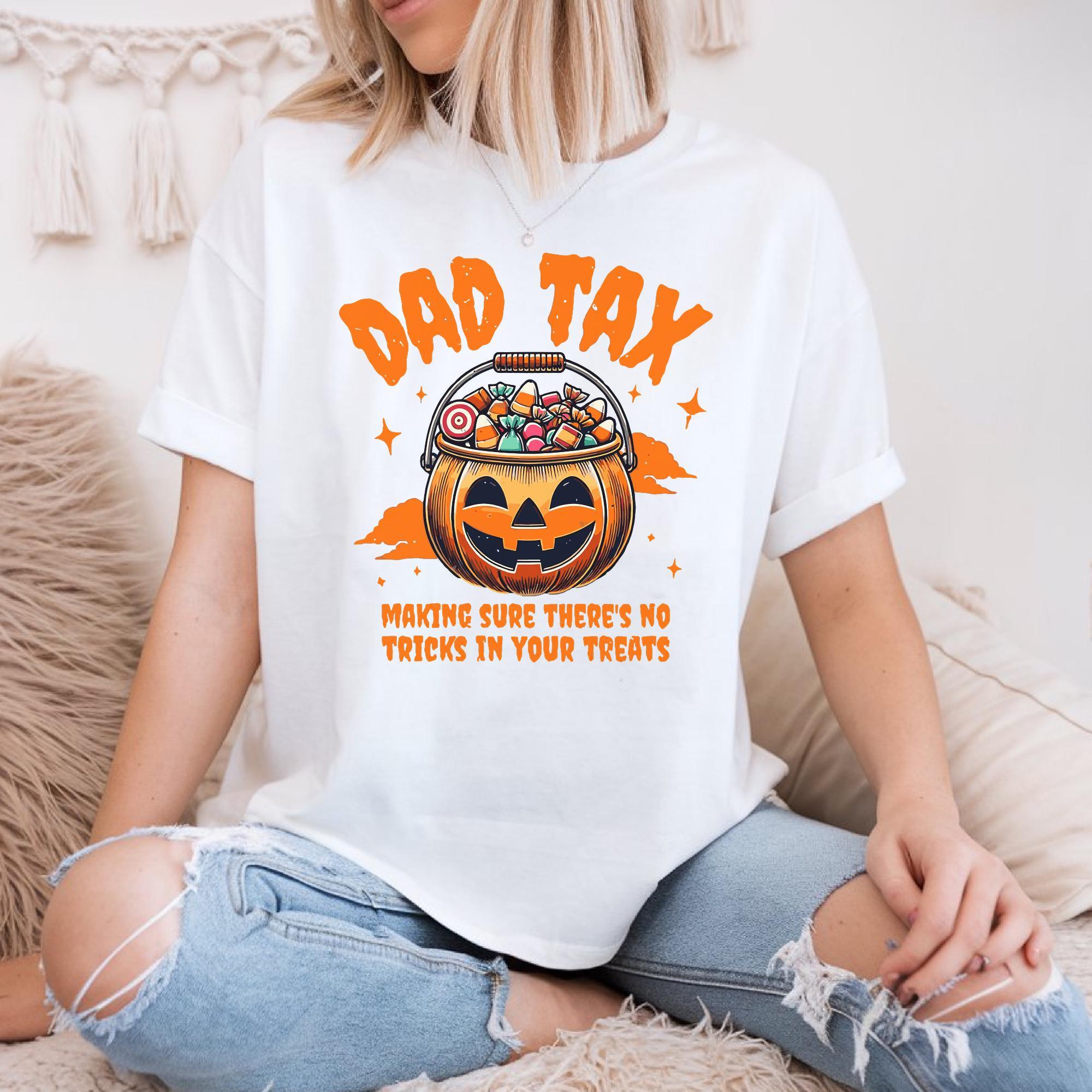 A woman wearing a white t-shirt with a graphic design of a jack-o-lantern and the text "DAD TAX" and "MAKING SURE THERE'S NO TRICKS IN YOUR TREATS" printed on it.