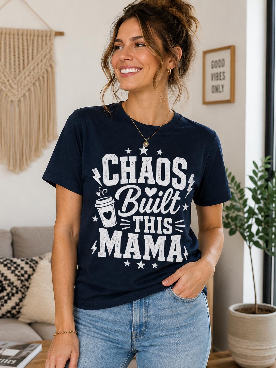 A woman wearing a navy blue t-shirt with the text "Chaos Built This Mama" is smiling and posing in a room with a potted plant and a wall decoration.