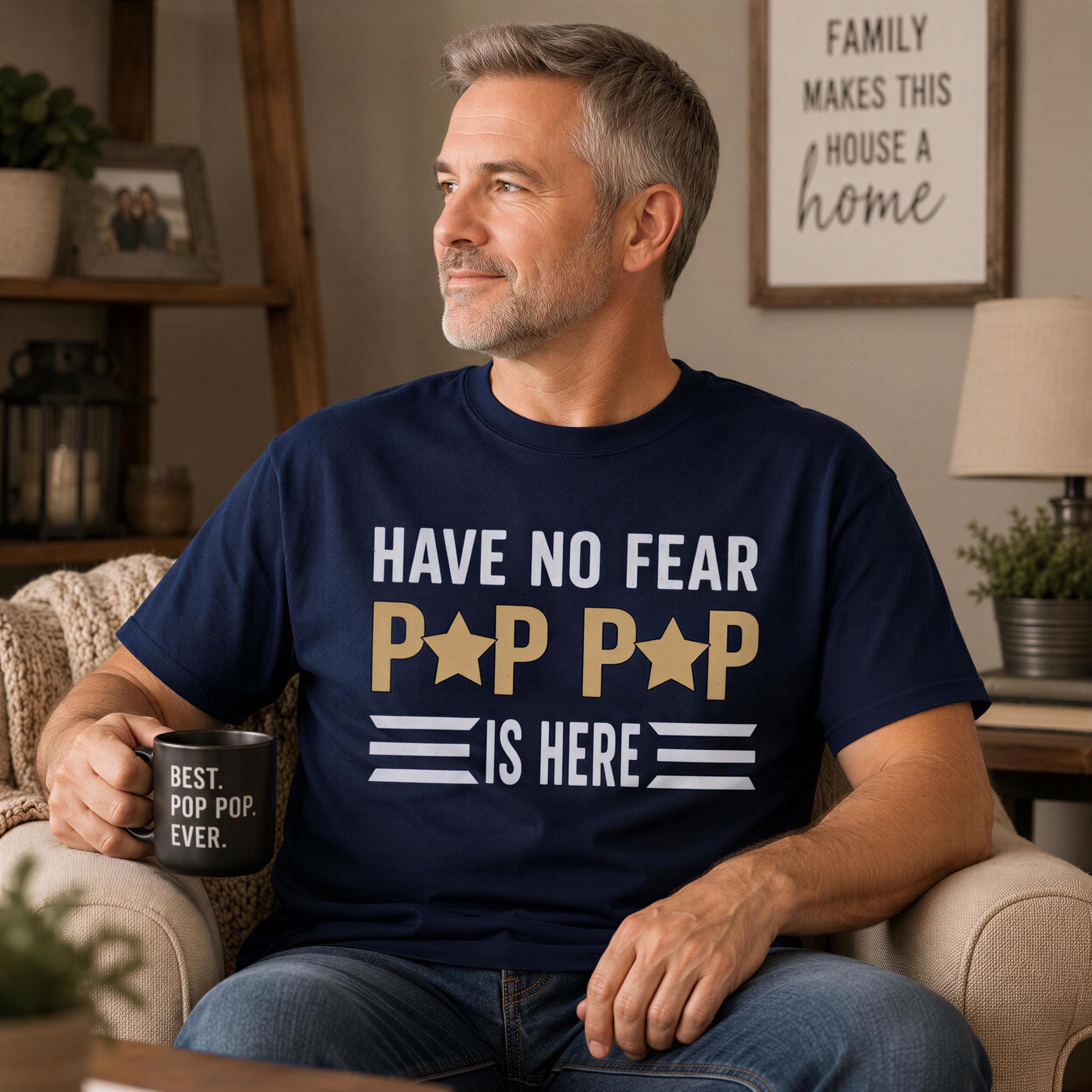 A man wearing a navy blue t-shirt with the text "HAVE NO FEAR POP POP IS HERE" is sitting on a couch, holding a black mug with the text "BEST POP POP EVER."