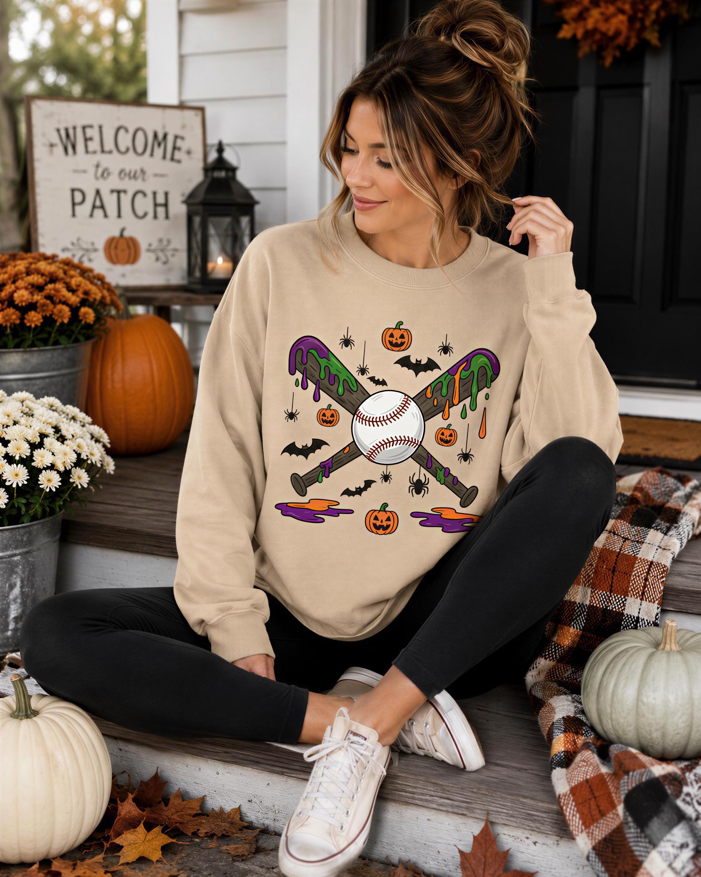 A woman sitting on a porch wearing a beige sweatshirt with a baseball graphic and Halloween decorations, including pumpkins and bats.
