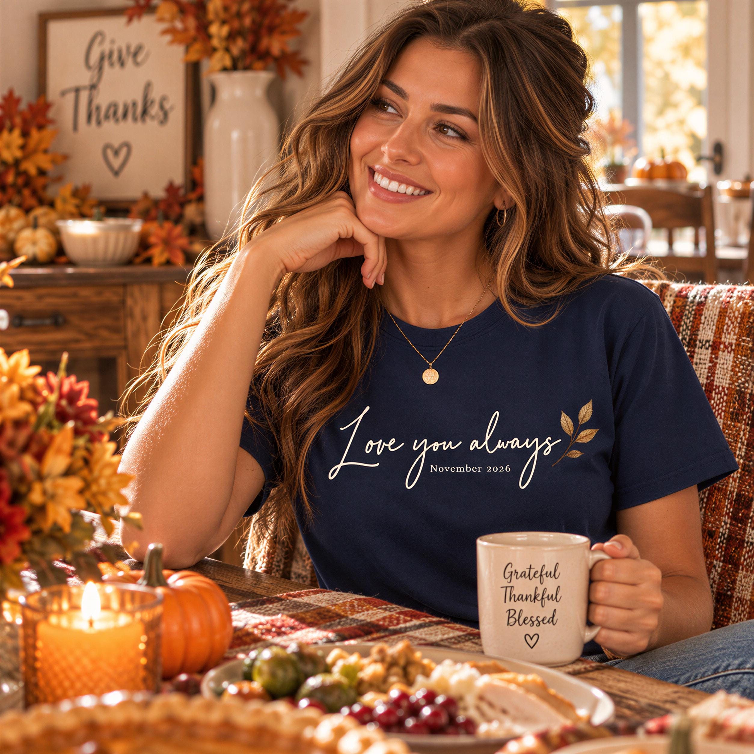A woman with long brown hair is sitting at a table, smiling and holding a coffee mug. The table is set with a plate of food, a candle, and a vase of flowers. The background includes a window and a sign that says "Give Thanks".