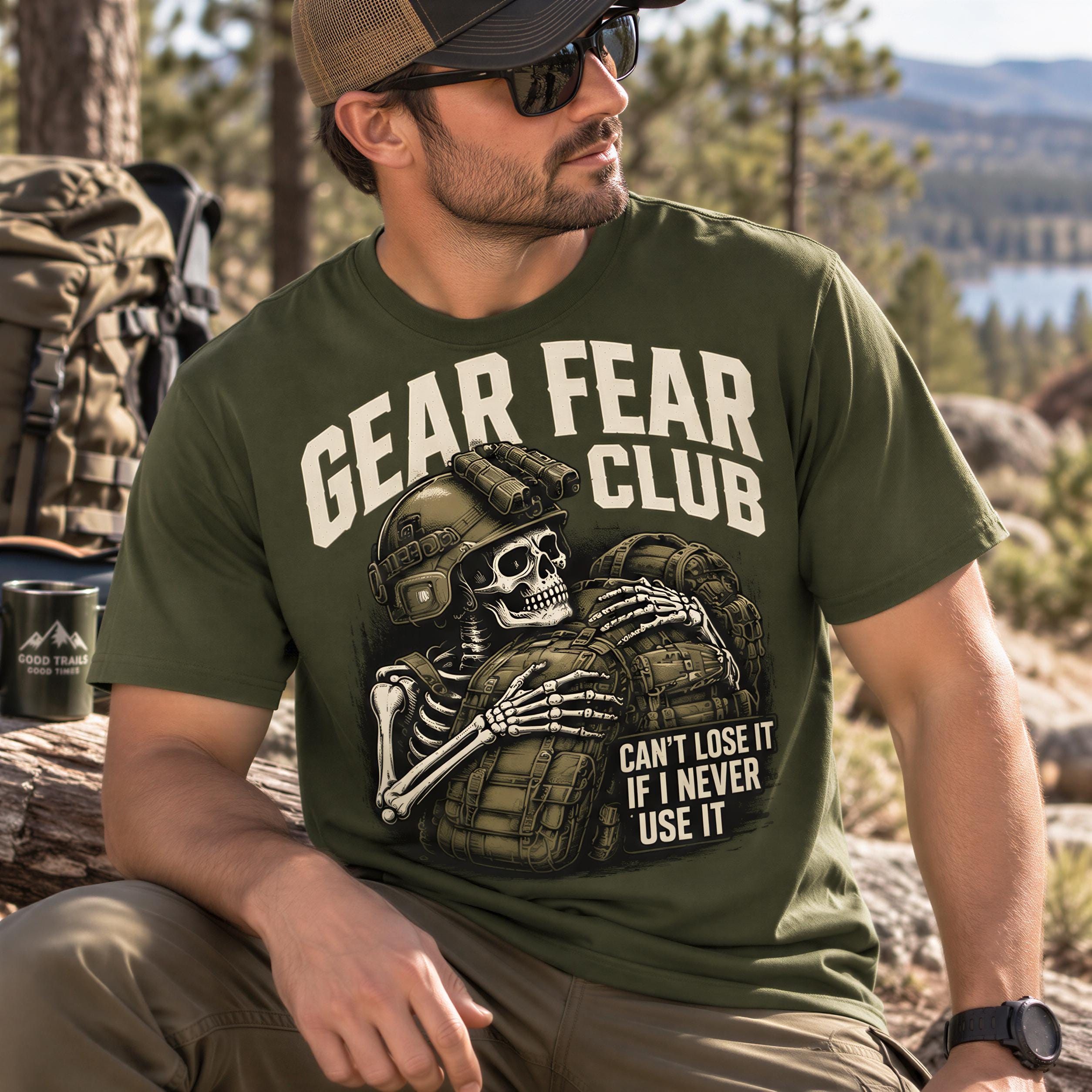 A man wearing a green t-shirt with a graphic of a skeleton and the text "GEAR FEAR CLUB" is sitting in a forested area.