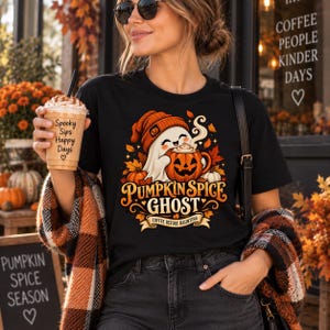 May include: A black t-shirt featuring a graphic of a white ghost wearing an orange beanie and holding a pumpkin mug. The text reads PUMPKIN SPICE GHOST COFFEE BEFORE HAUNTING. The design includes autumn leaves and pumpkins in orange and brown tones.