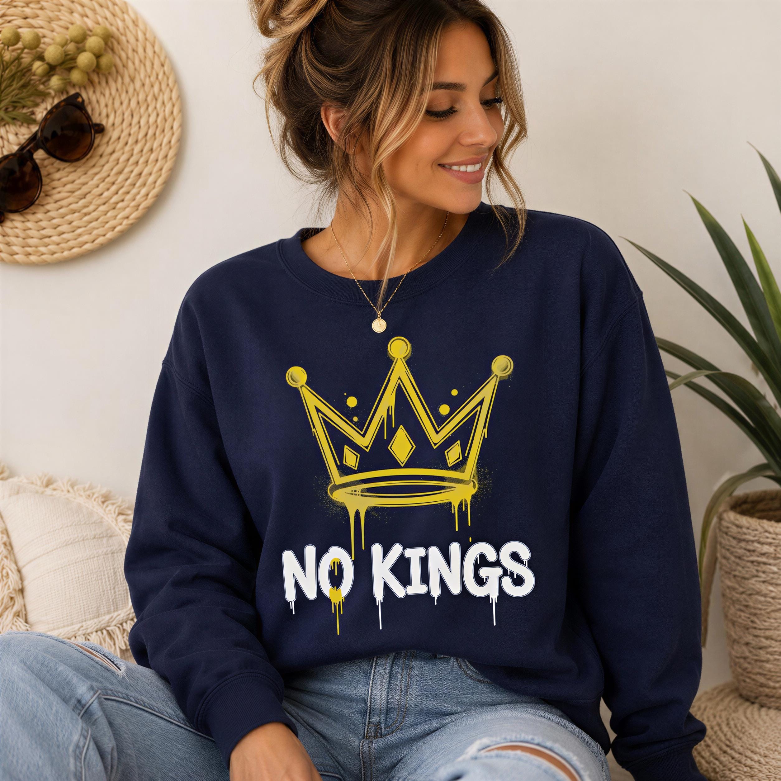 A woman wearing a navy blue sweatshirt with a yellow crown graphic and the text "NO KINGS" printed on it, smiling and looking down.