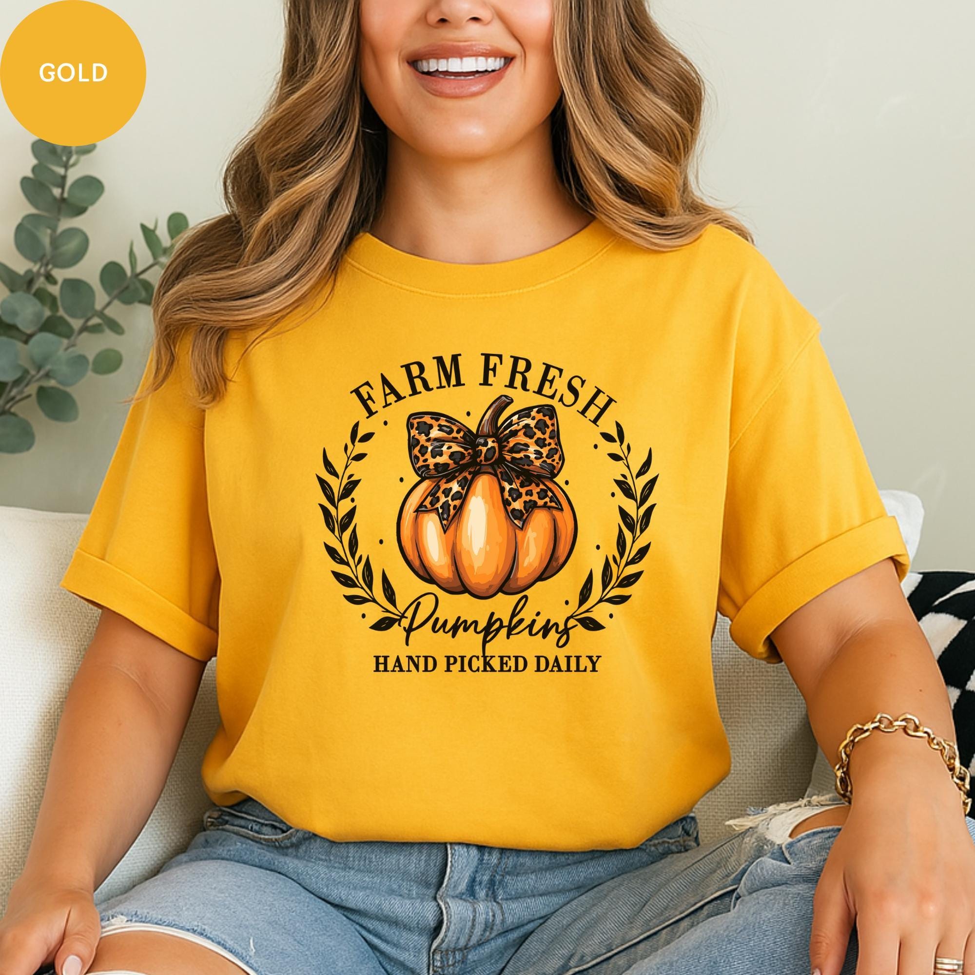 A woman wearing a yellow t-shirt with a pumpkin graphic and text, smiling and sitting on a couch.