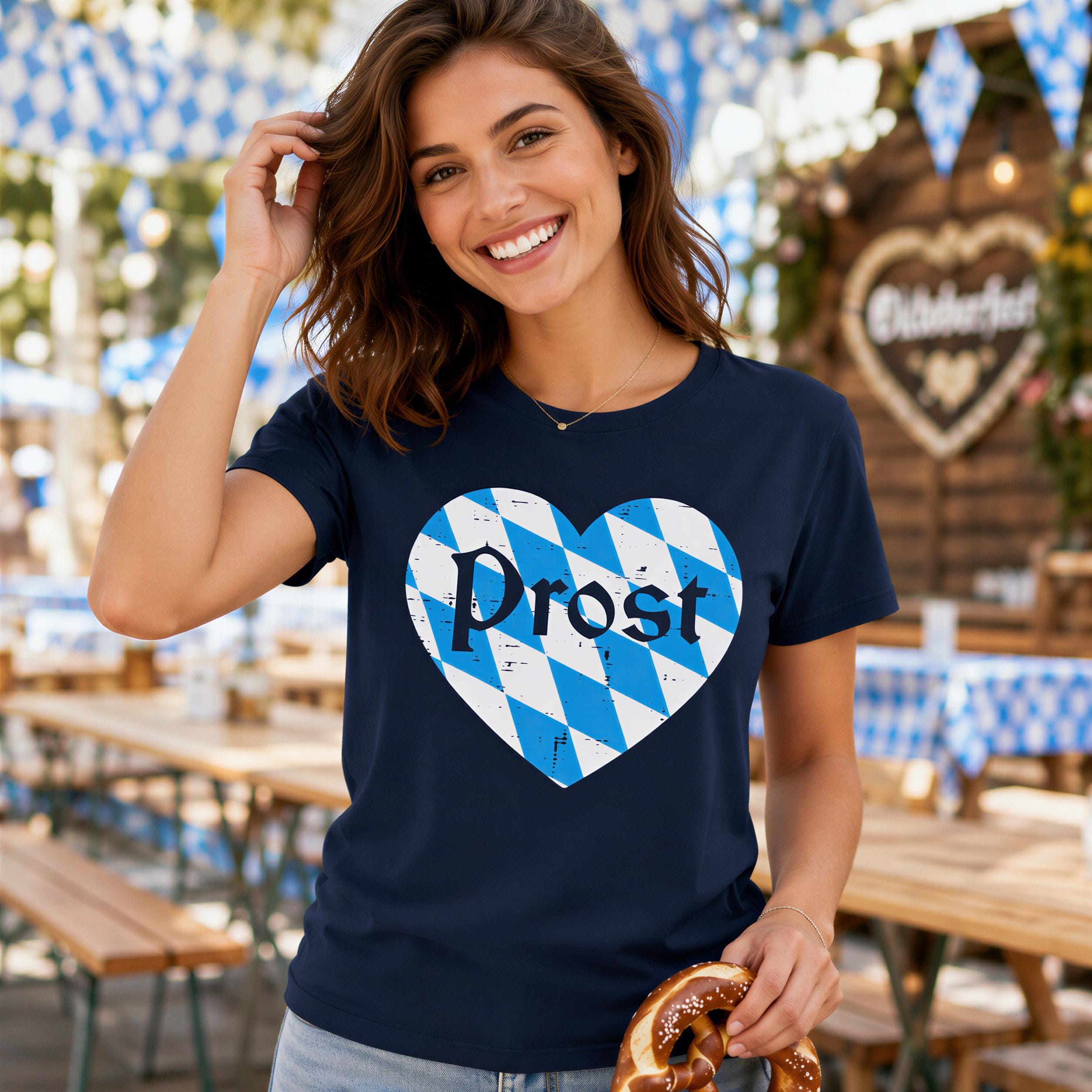 A smiling woman wearing a navy blue t-shirt with a heart-shaped graphic and the word "Prost" printed on it, holding a pretzel.