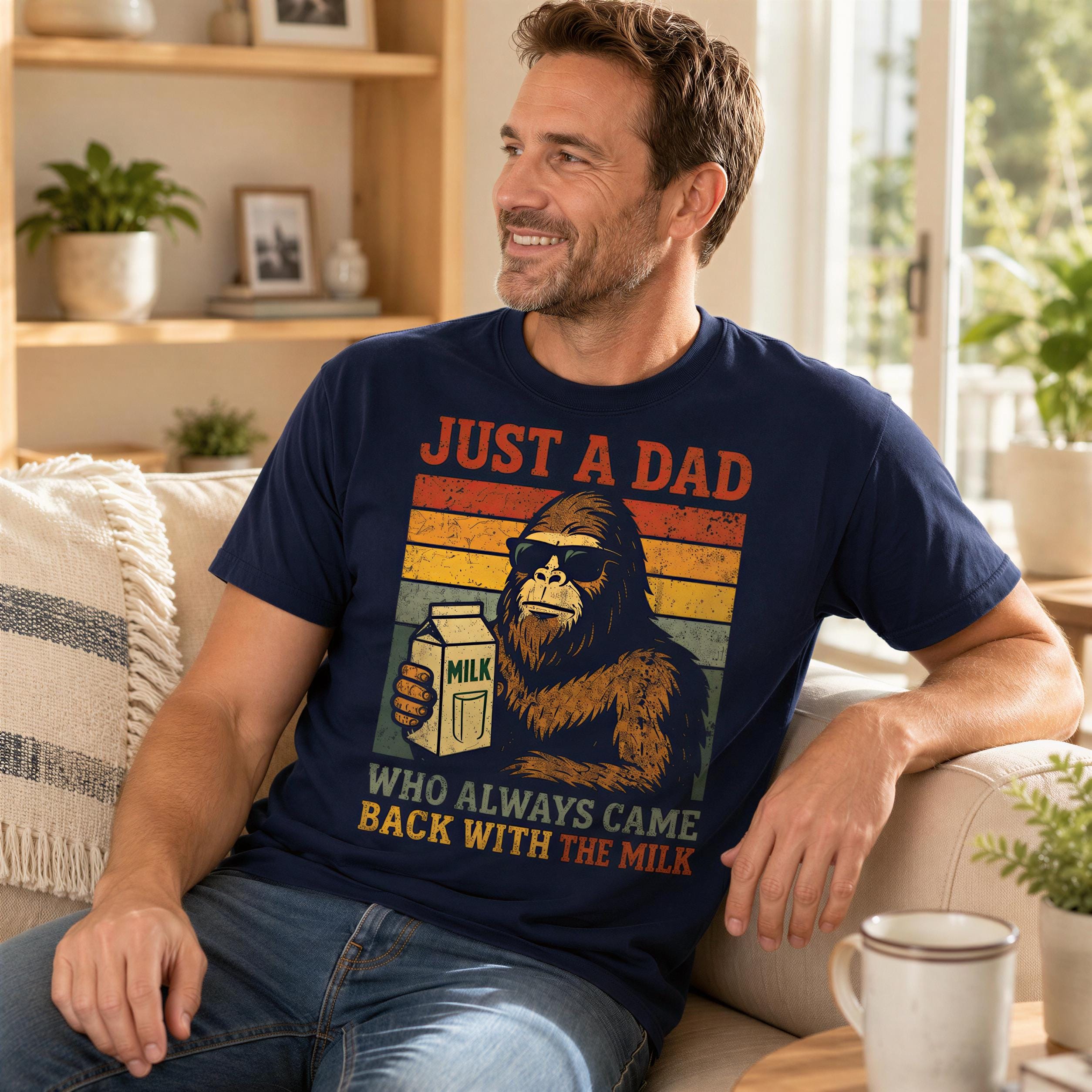 A man wearing a blue t-shirt with a graphic of a gorilla holding a carton of milk and the text "Just a Dad" is sitting on a couch in a living room.