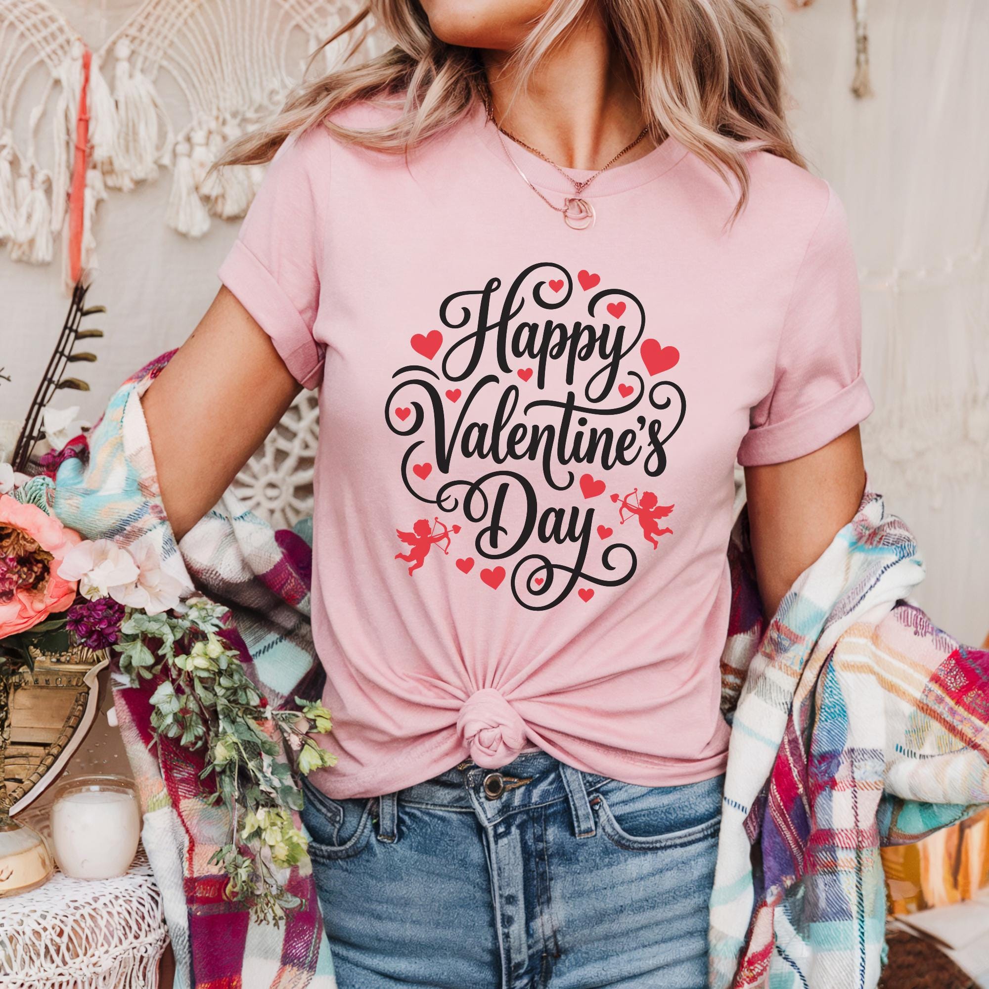 A woman wearing a pink t-shirt with the text "Happy Valentine's Day" printed on it, standing in front of a floral arrangement.