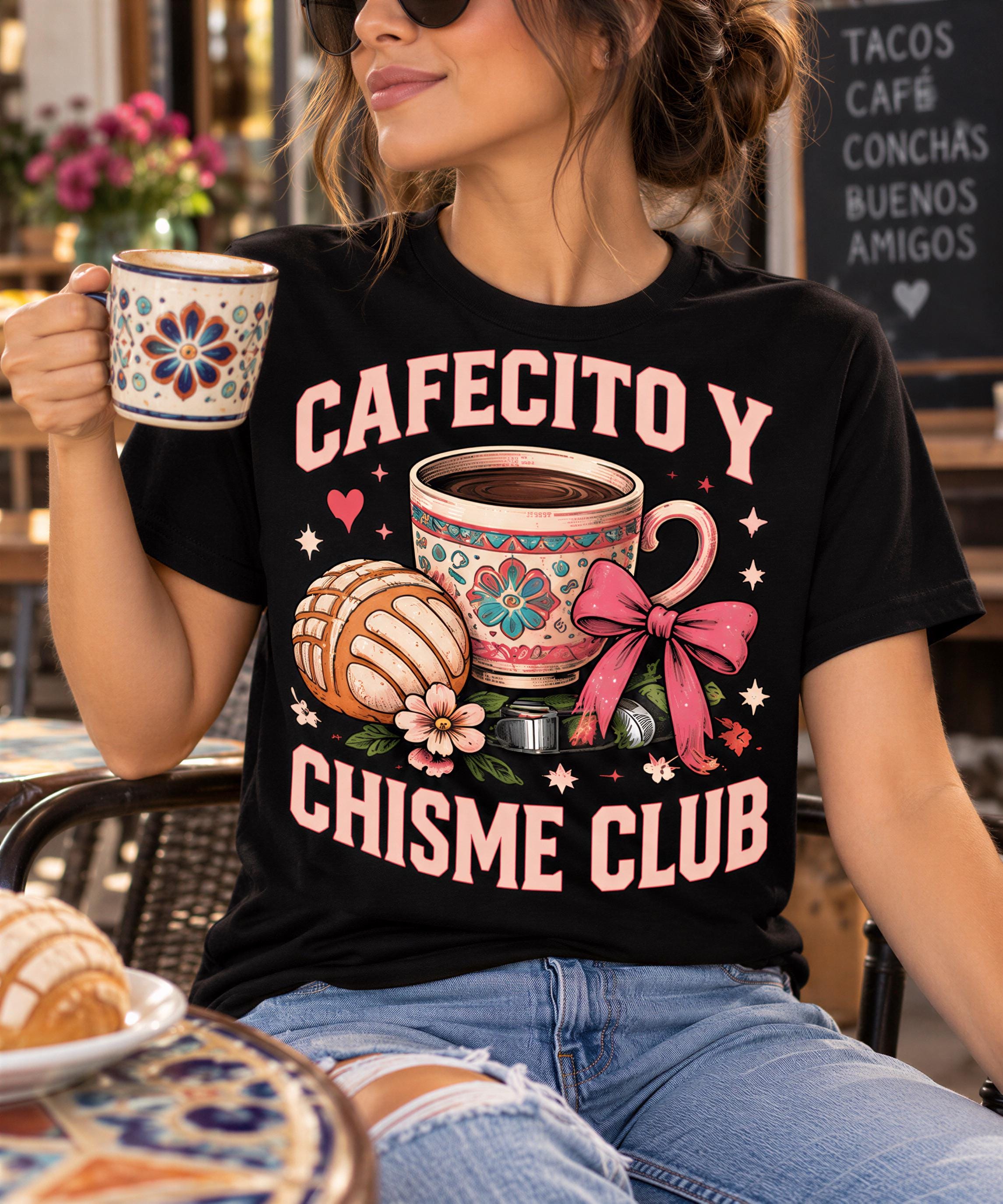 A woman wearing a black t-shirt with a graphic design of a coffee cup and other decorative elements, sitting at a table with a cup of coffee in her hand.