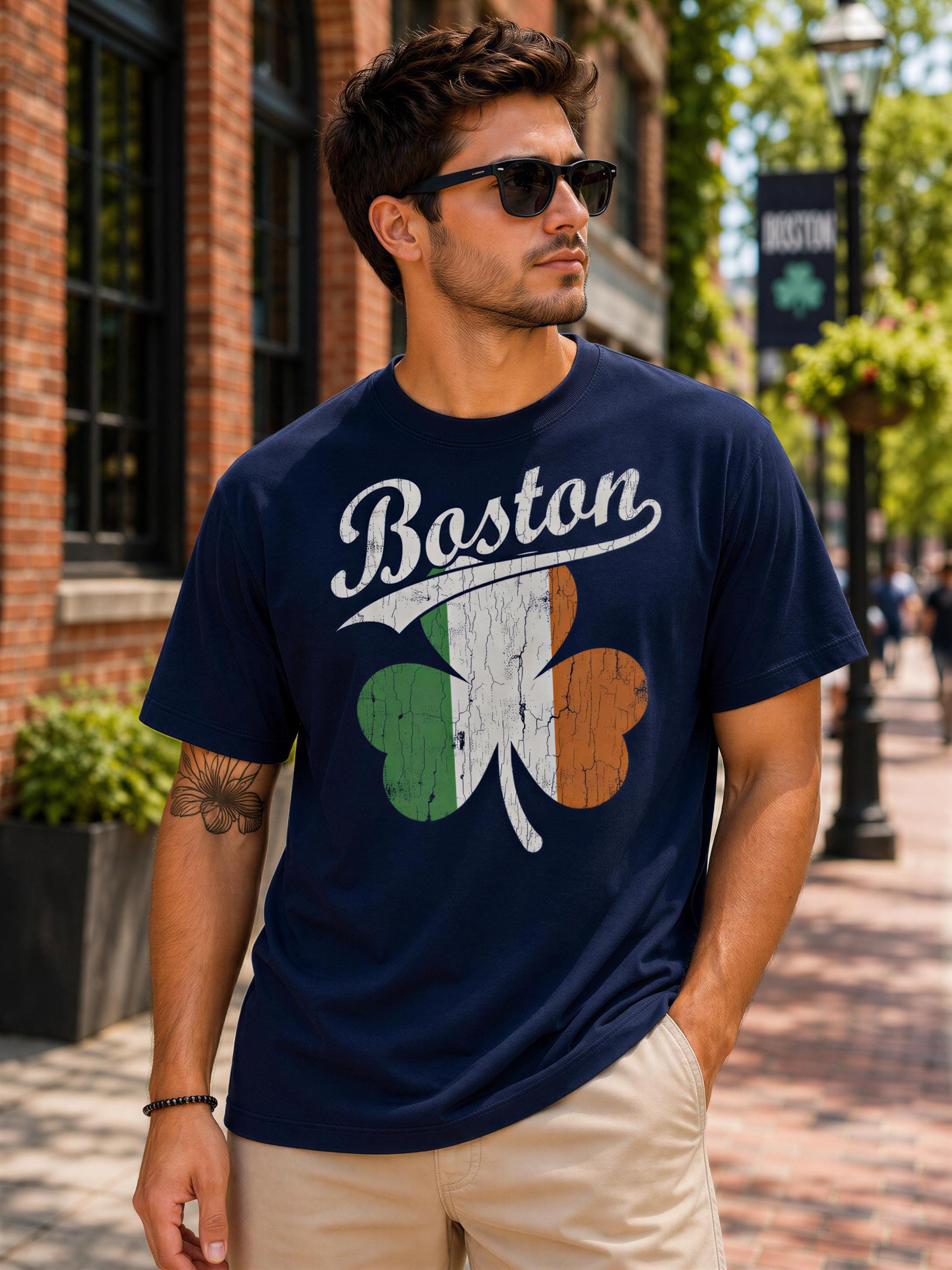 A man wearing a navy blue t-shirt with a graphic of a clover and the word "Boston" printed on it, standing on a city street.