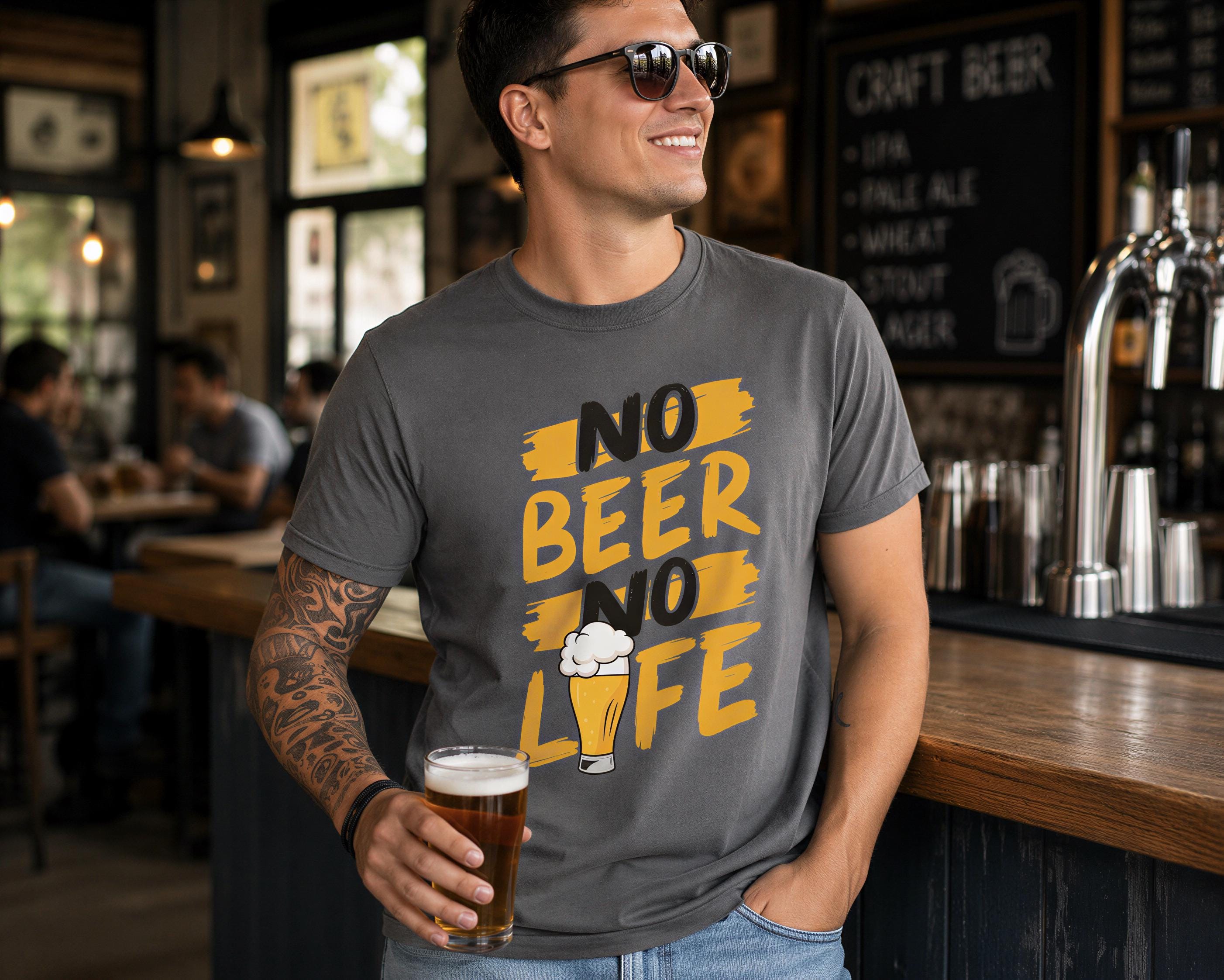 A man wearing a gray t-shirt with a graphic design and holding a glass of beer stands in a bar.