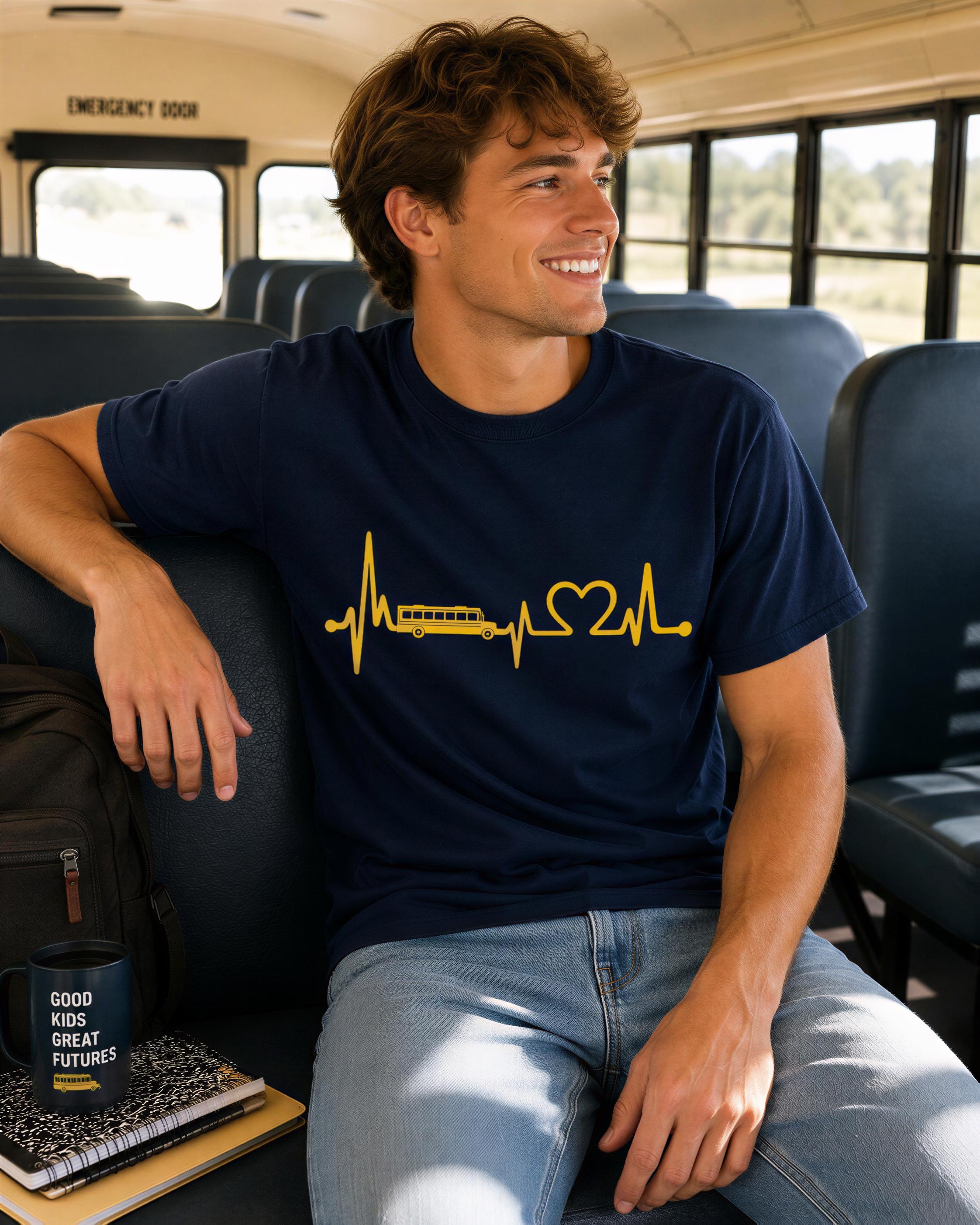 A young man wearing a navy blue t-shirt with a yellow heart-shaped line graphic and a bus symbol is sitting on a bus seat, smiling and looking to the side.