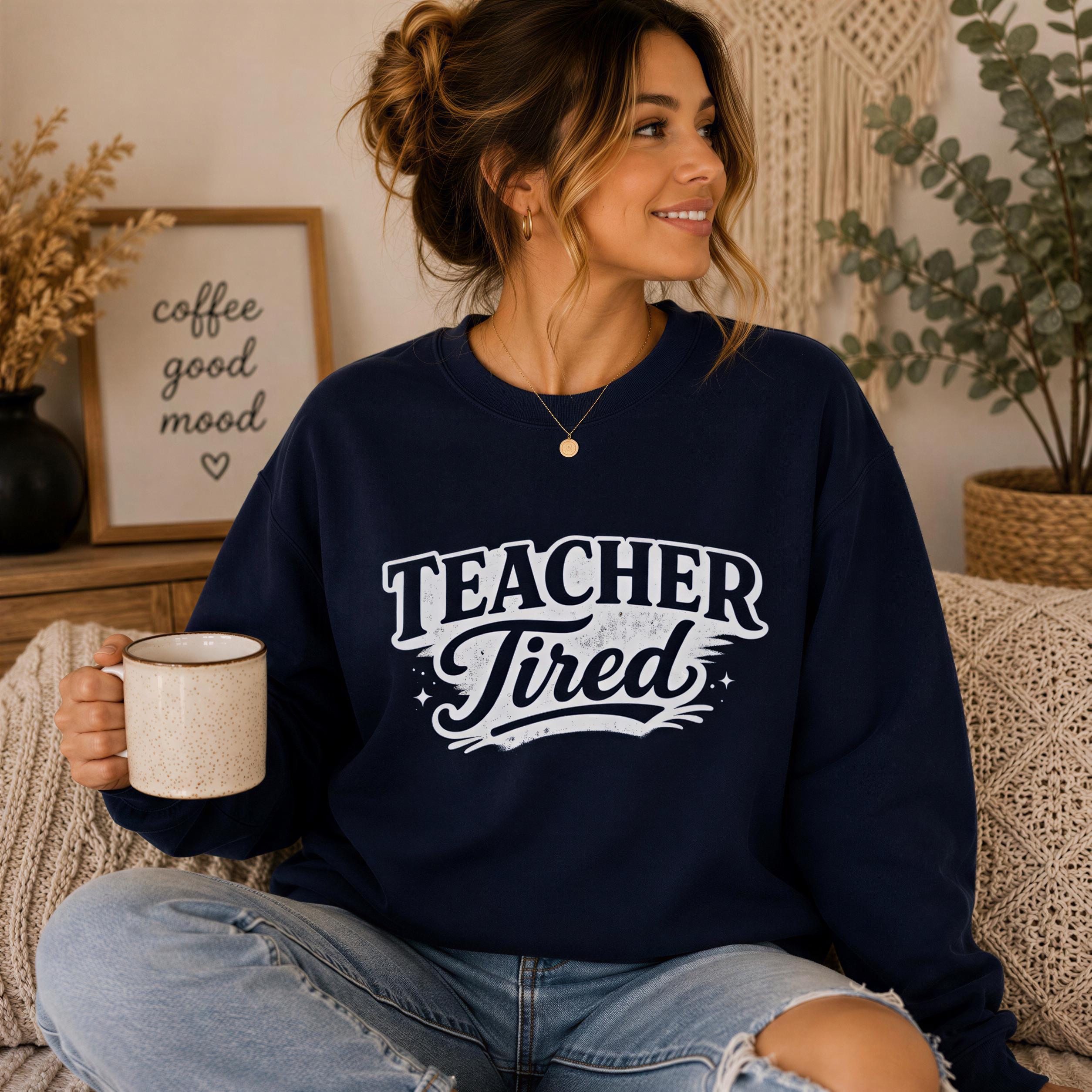 A woman wearing a navy blue sweatshirt with the text "TEACHER TIRED" is sitting on a couch, holding a coffee mug and smiling.