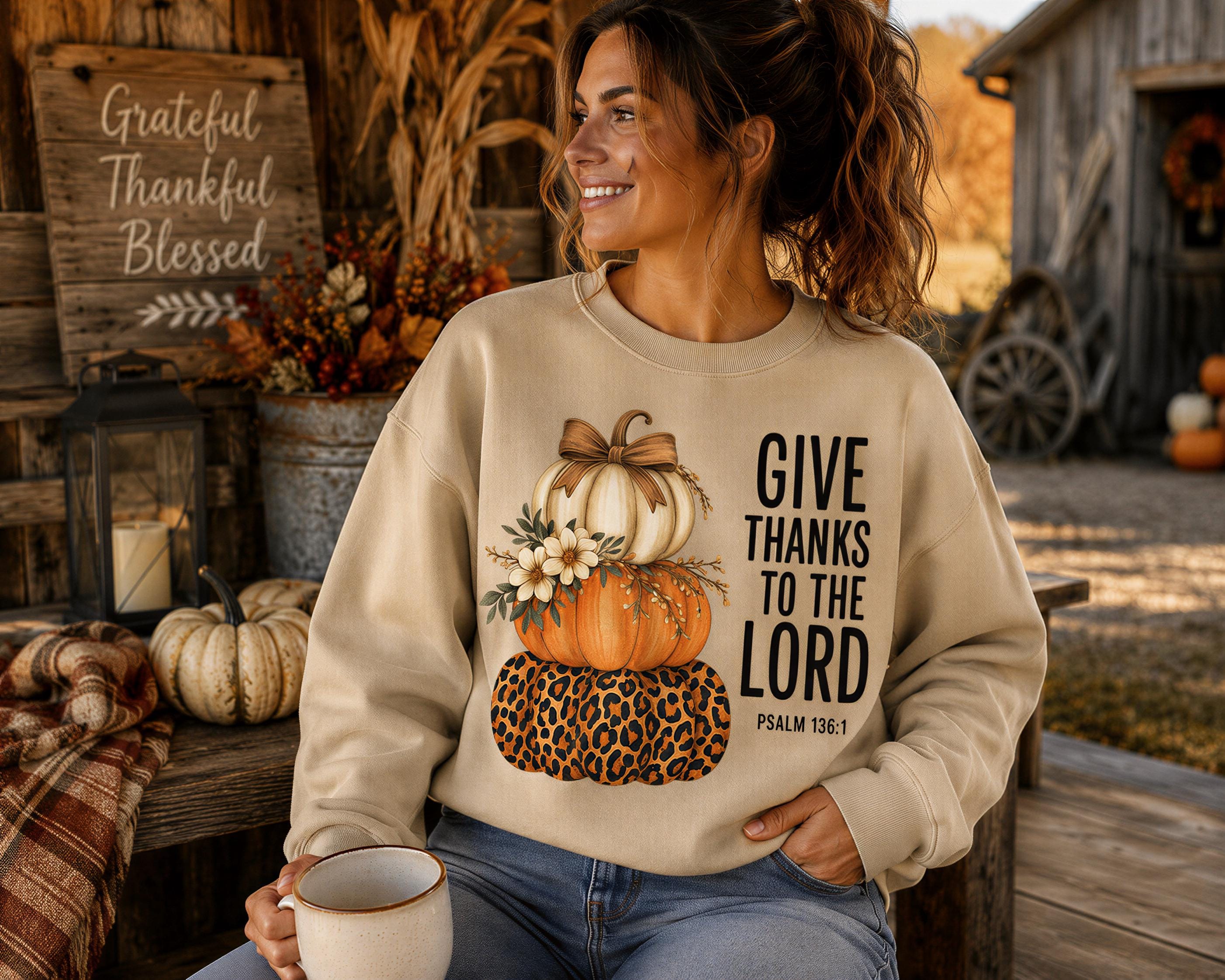 A woman wearing a sweatshirt with a pumpkin and leopard print design, sitting on a bench and holding a coffee mug, with a rustic wooden structure and fall decorations in the background.