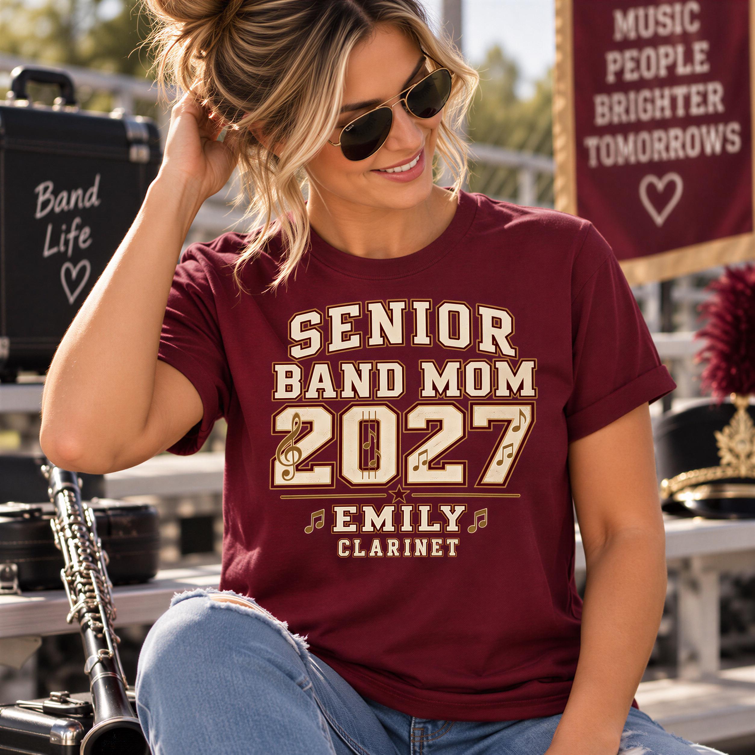 A woman wearing a burgundy t-shirt with the text "SENIOR BAND MOM 2027 EMILY CLARINET" is sitting on a bench, smiling and looking at the camera.