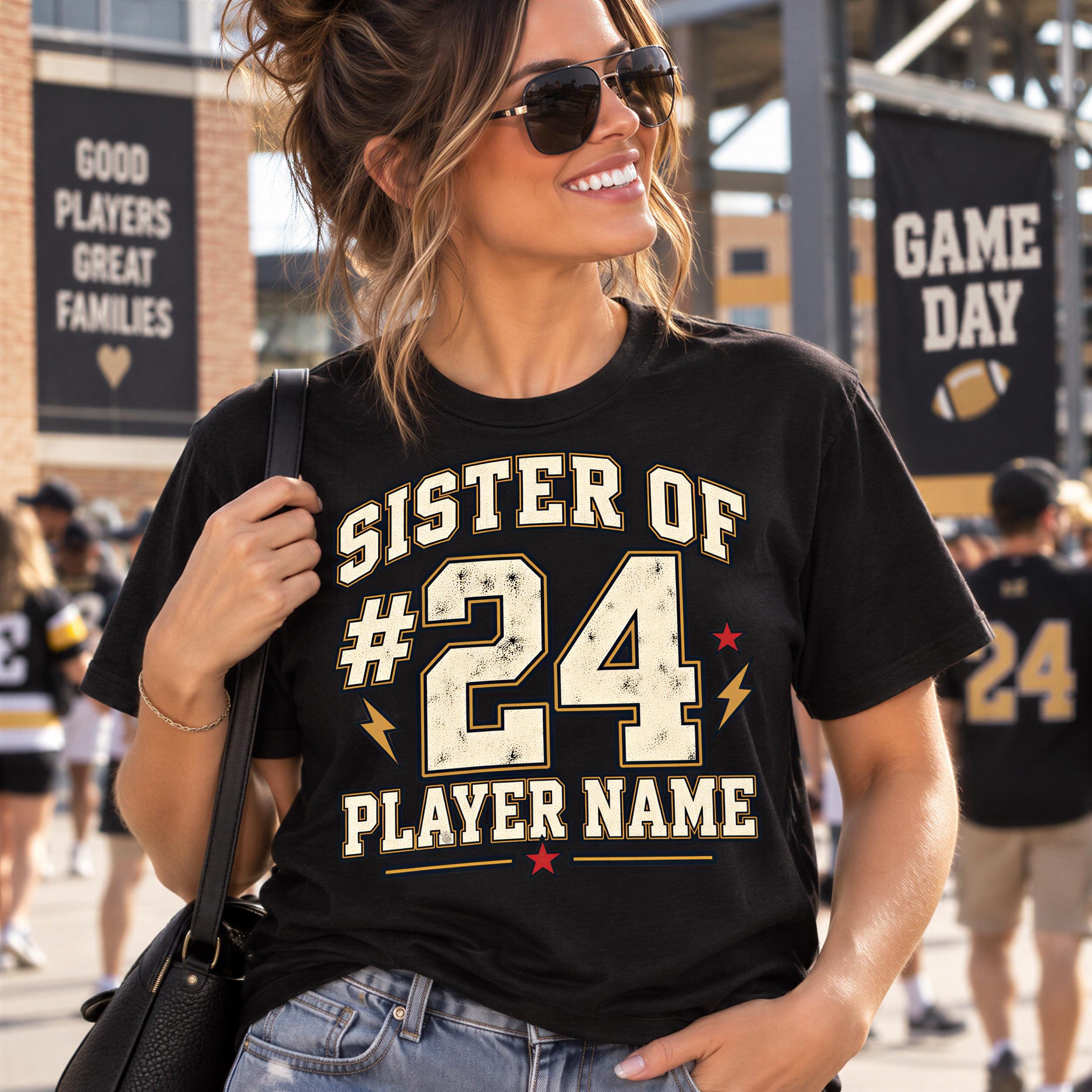 A woman wearing a black t-shirt with the text "SISTER OF #24 PLAYER NAME" printed on it, smiling and holding a black purse.