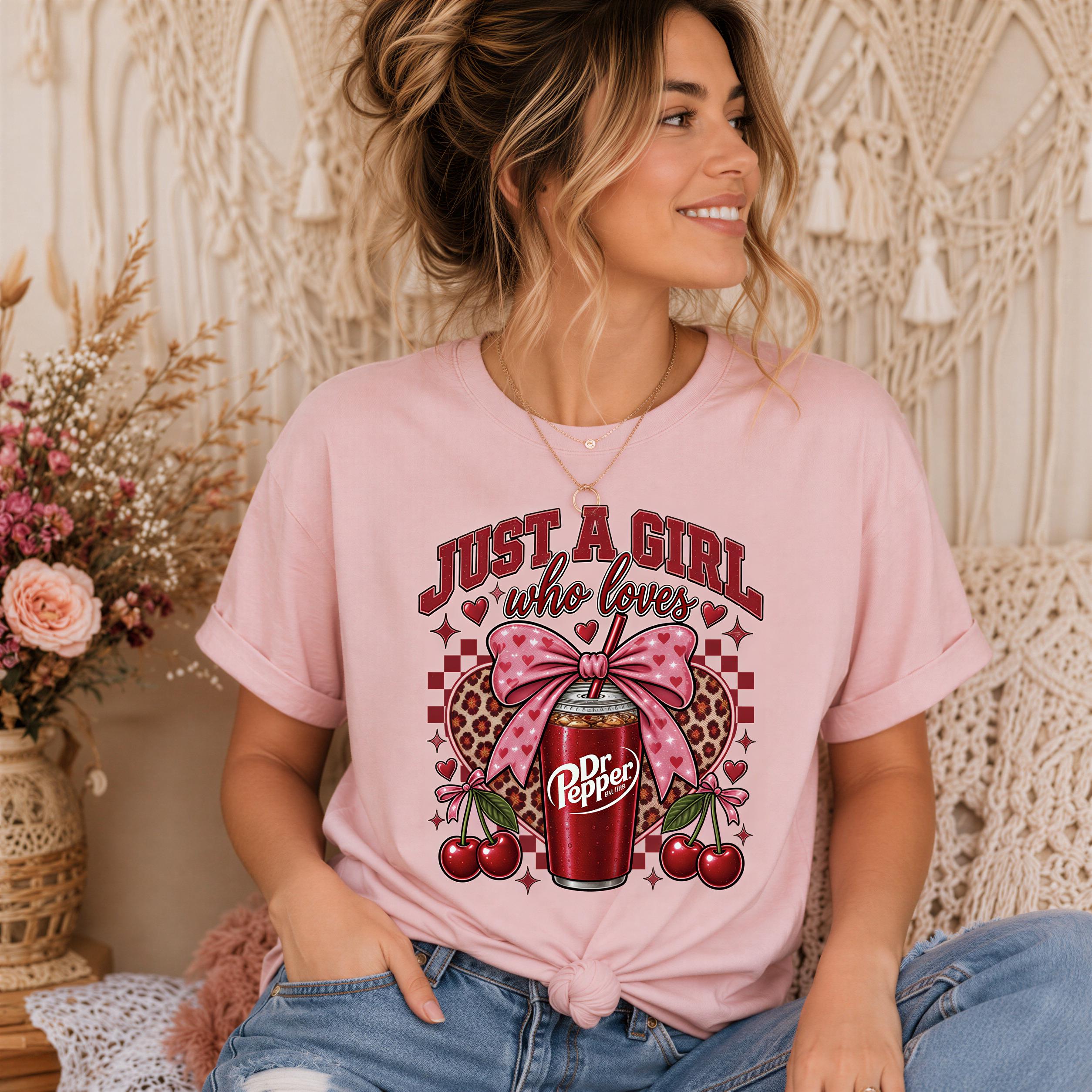 A woman wearing a pink t-shirt with a graphic design of a soda can and various decorative elements, including a bow and cherries.