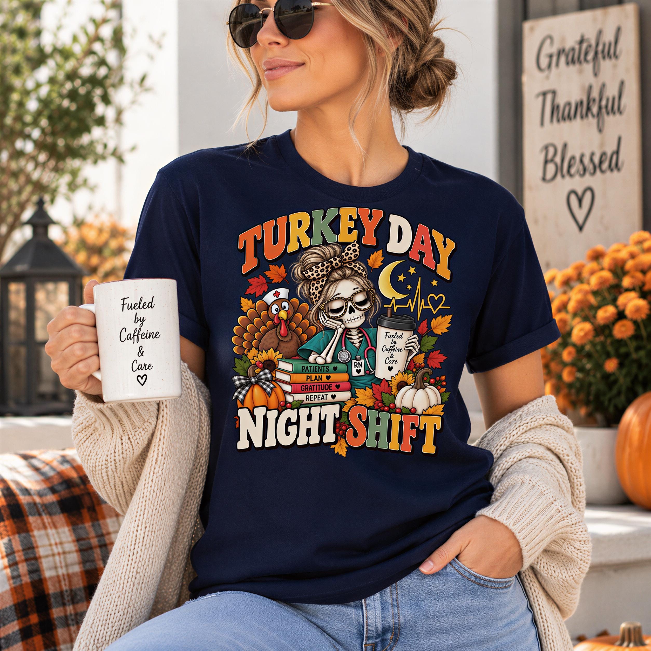 A woman wearing a blue t-shirt with a turkey-themed design and holding a coffee mug, sitting on a porch with fall decorations in the background.