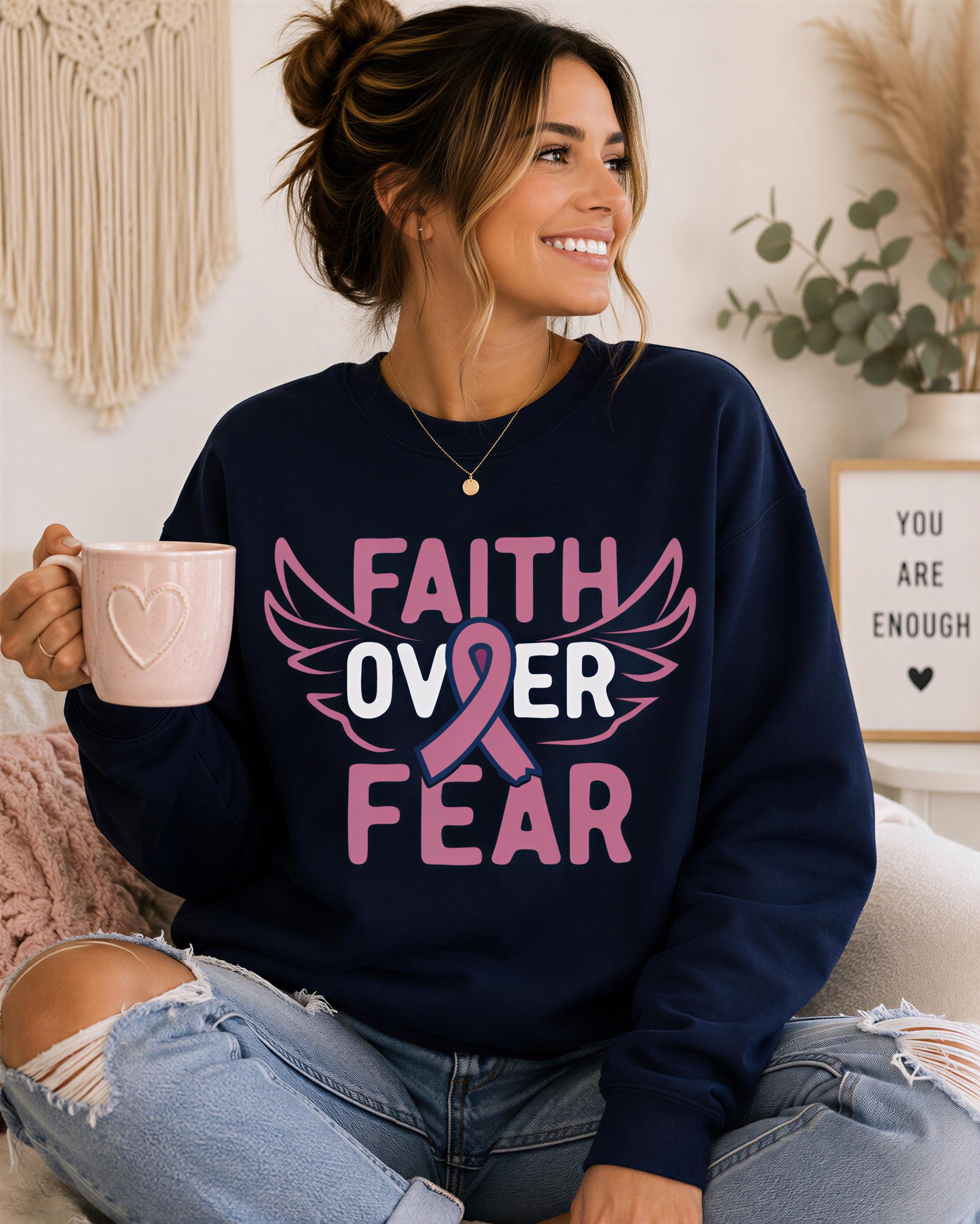 A woman wearing a navy blue sweatshirt with pink text and a pink ribbon design, holding a pink mug, and smiling.